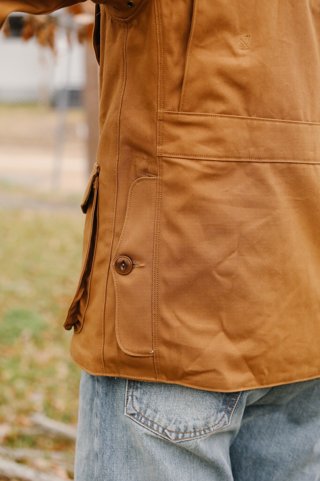 Close-up of a person wearing a brown jacket with a blurred outdoor background