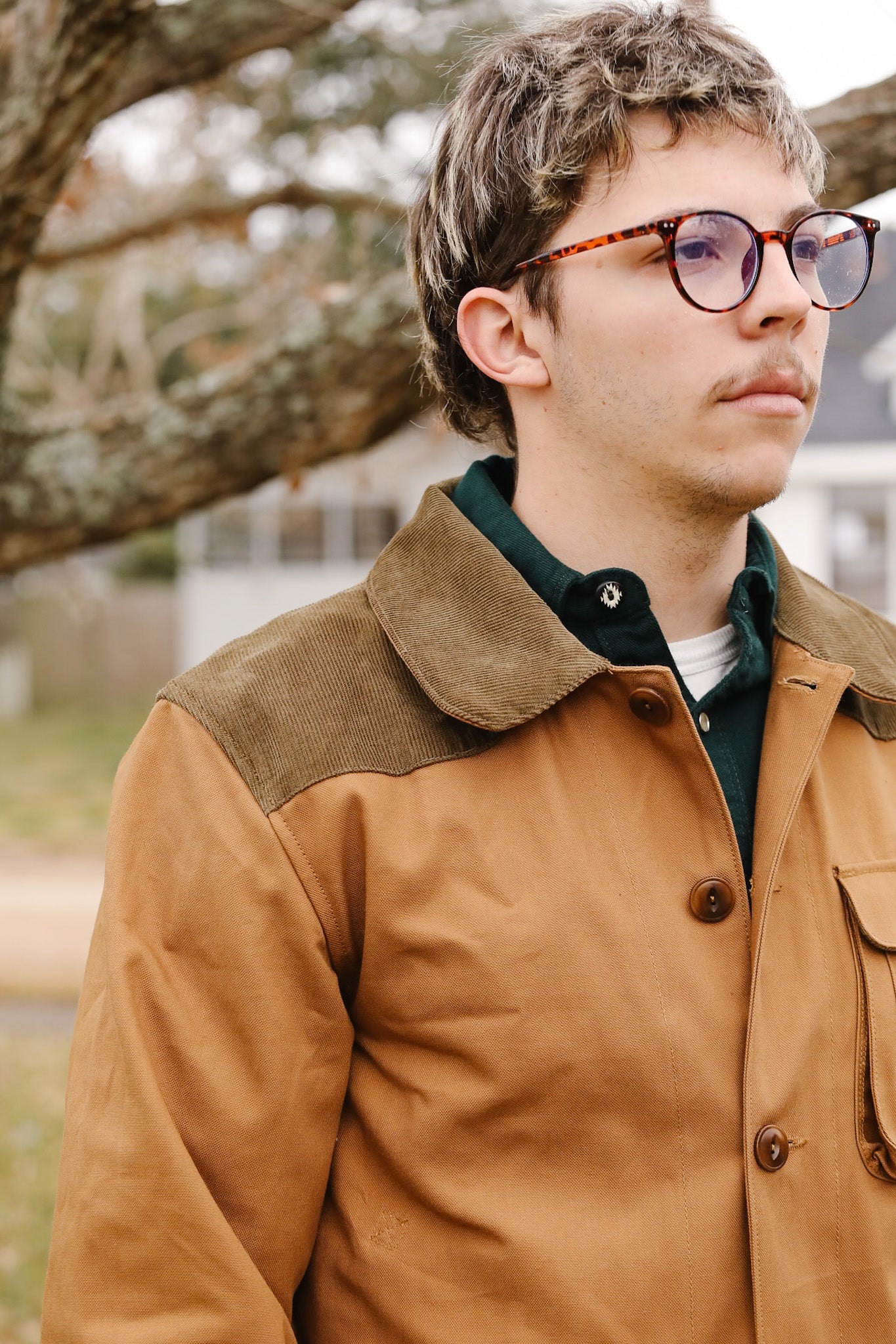 Man wearing a brown jacket with a tree in the background