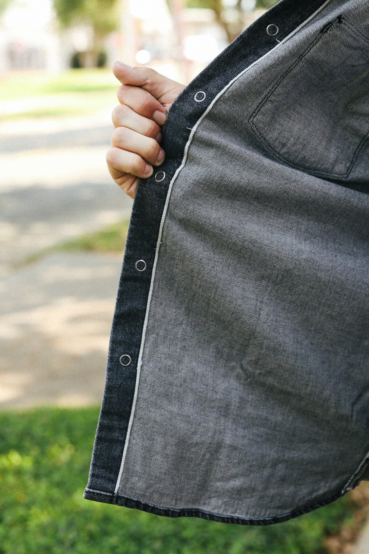 Close-up of a person holding a dark gray jacket with a blurred outdoor background