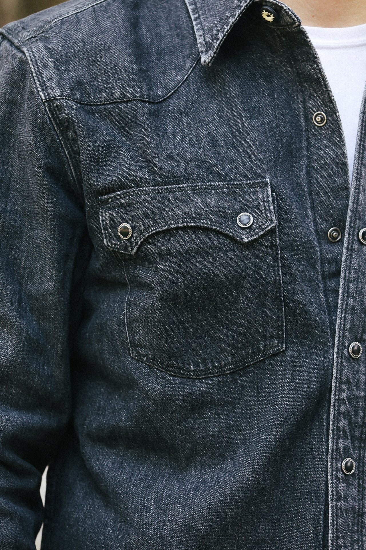 Close-up of a dark denim shirt with a pocket and buttons.