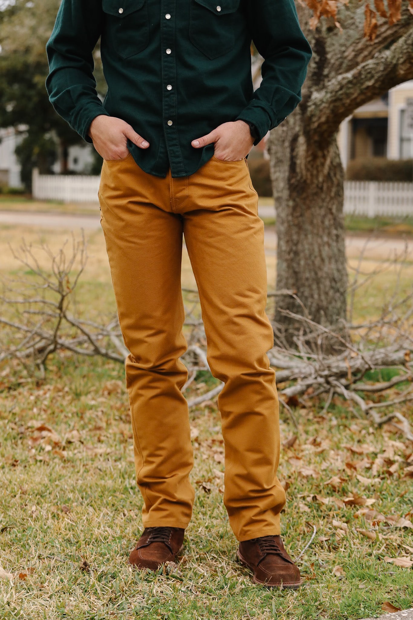 Person wearing a green shirt and mustard yellow pants standing outdoors with trees and grass in the background.