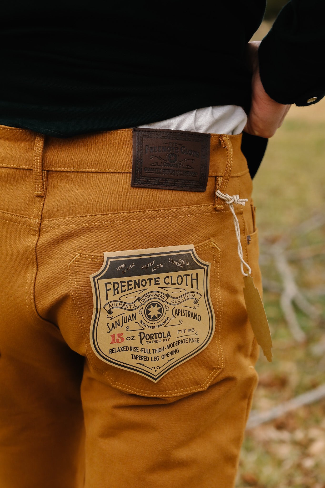 Brown pants with a visible brand label on the back pocket, set against a blurred natural background.