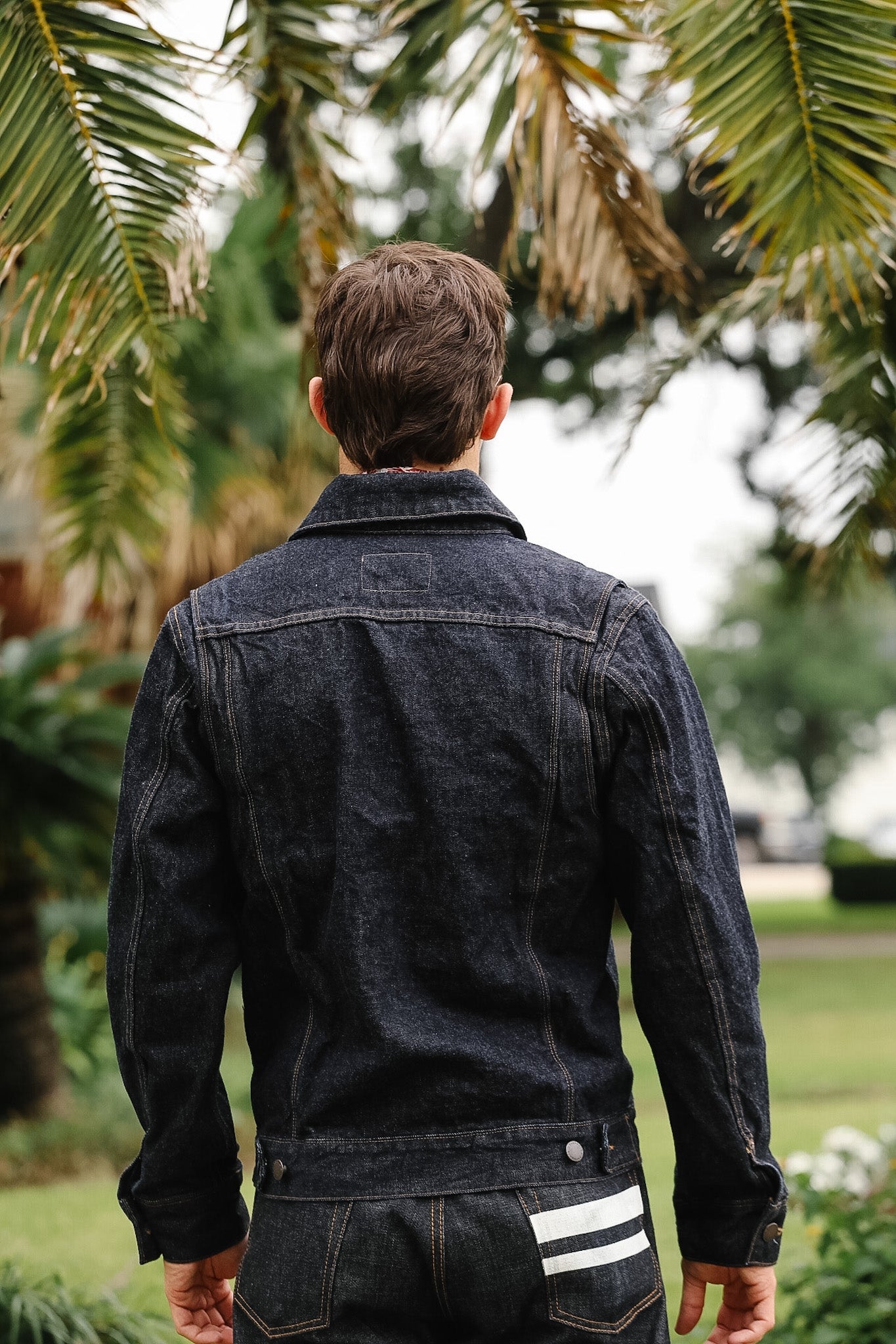 Man wearing a dark denim jacket with a blurred outdoor background