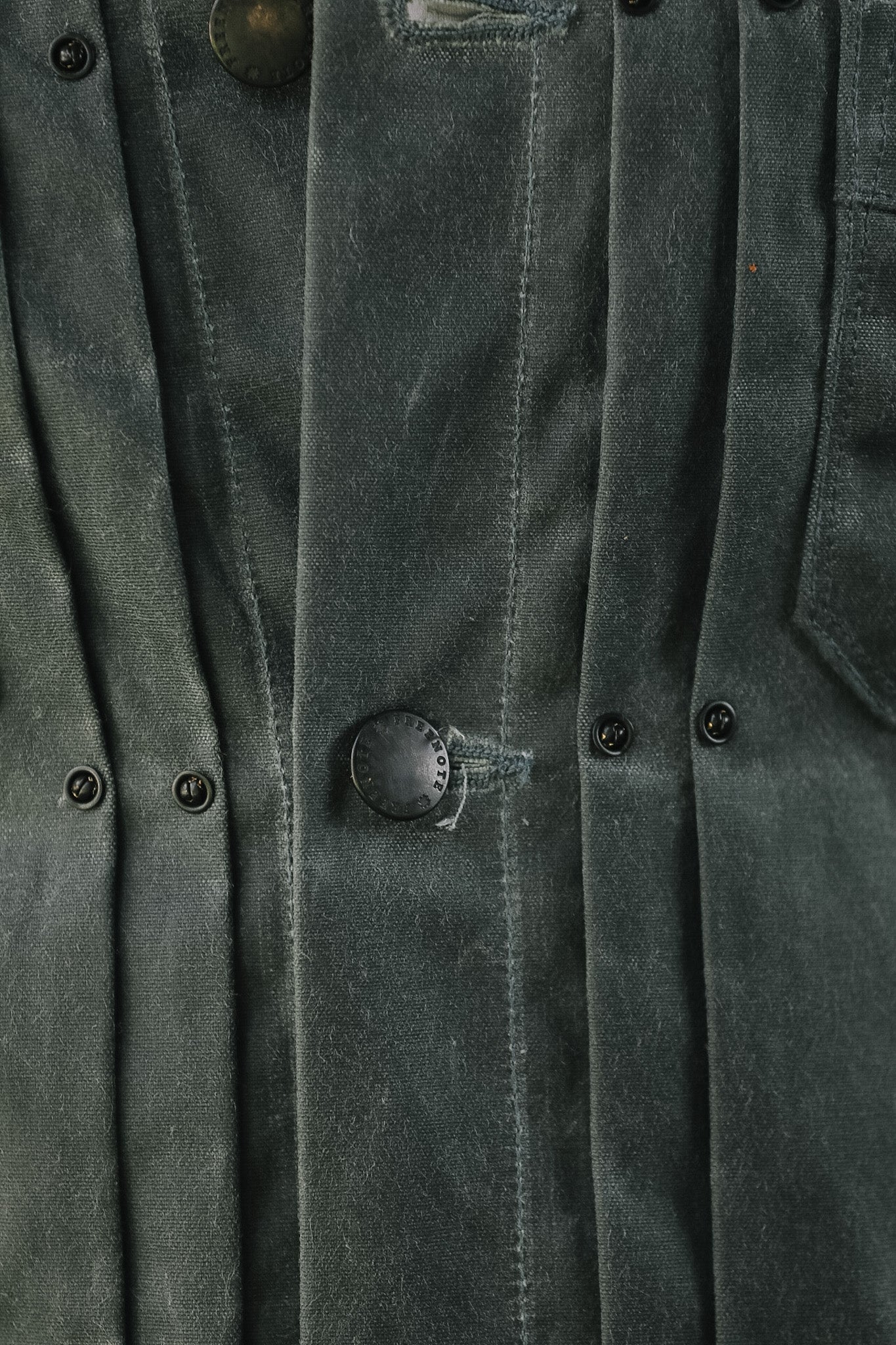 Close-up of a dark gray textured jacket or overshirt with vertical pleats, button closures, and visible fabric wear.