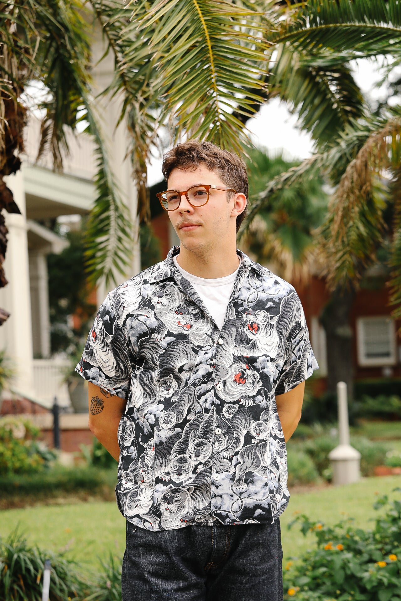 Man wearing a patterned shirt standing outdoors with greenery in the background