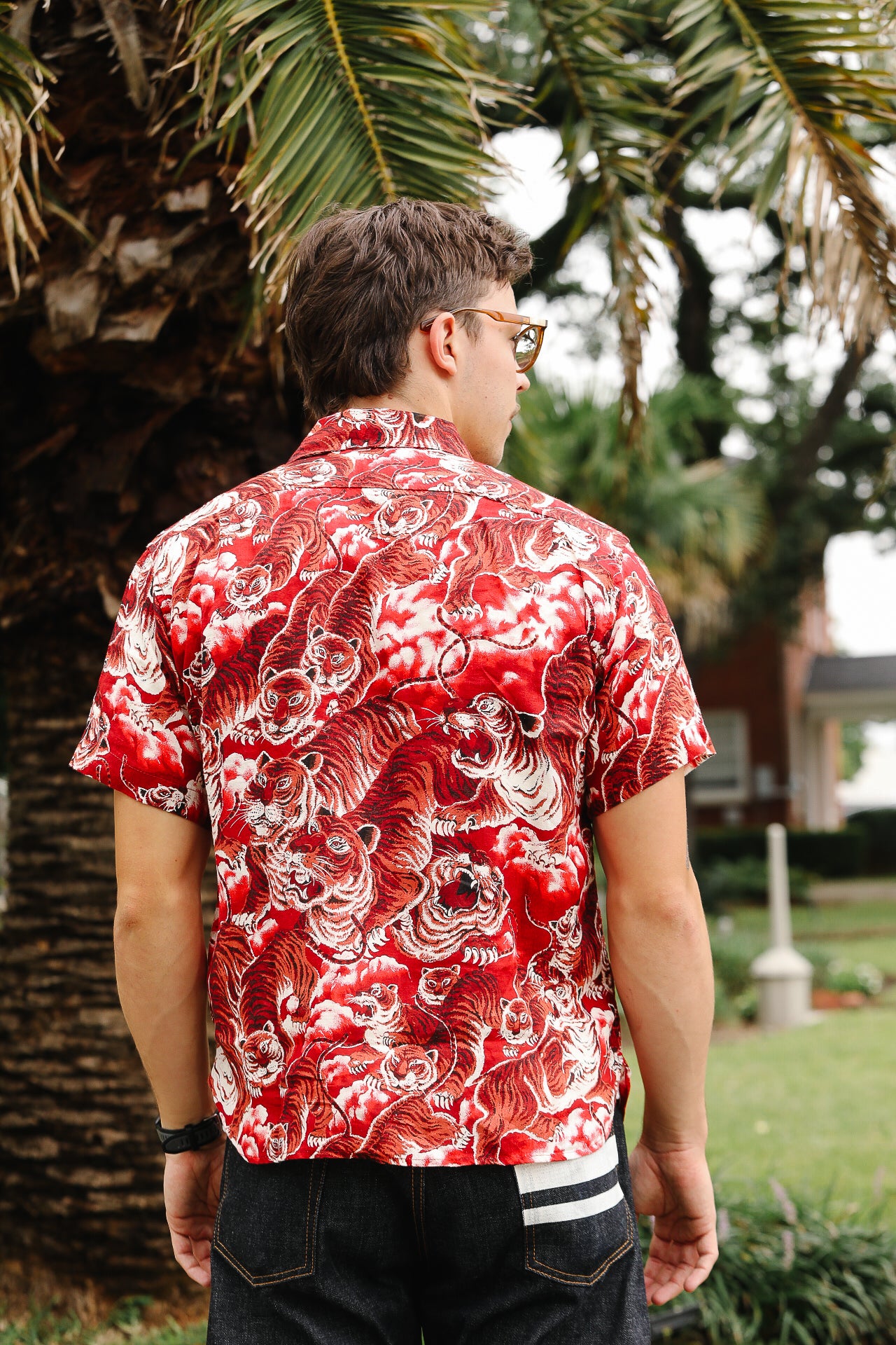 Person wearing a red and white patterned shirt in an outdoor setting with palm trees.