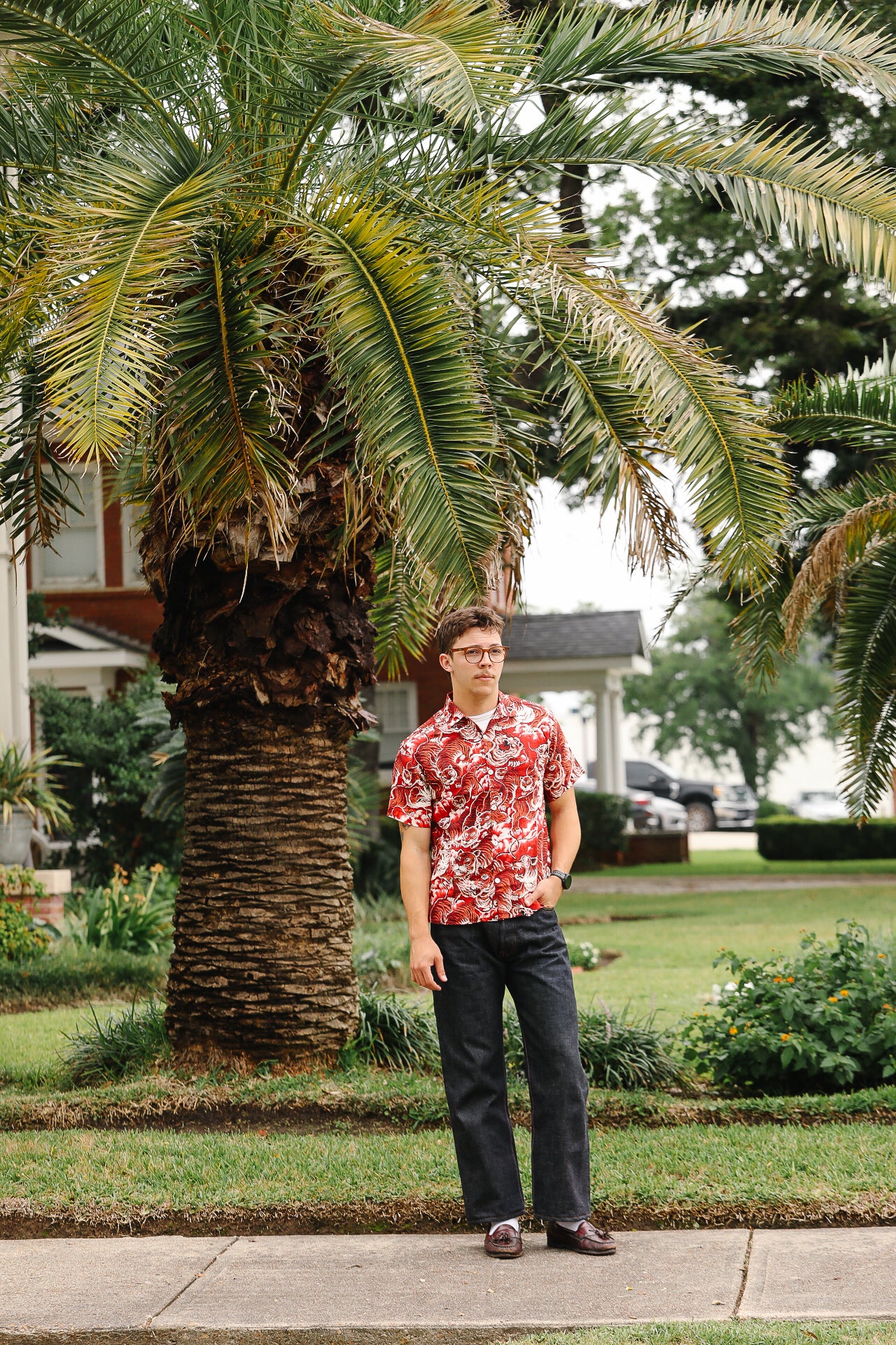 Man in a red patterned shirt standing in front of a palm tree