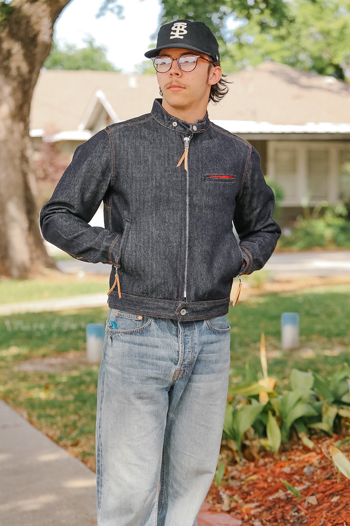 Person wearing a dark denim jacket and jeans standing outdoors.