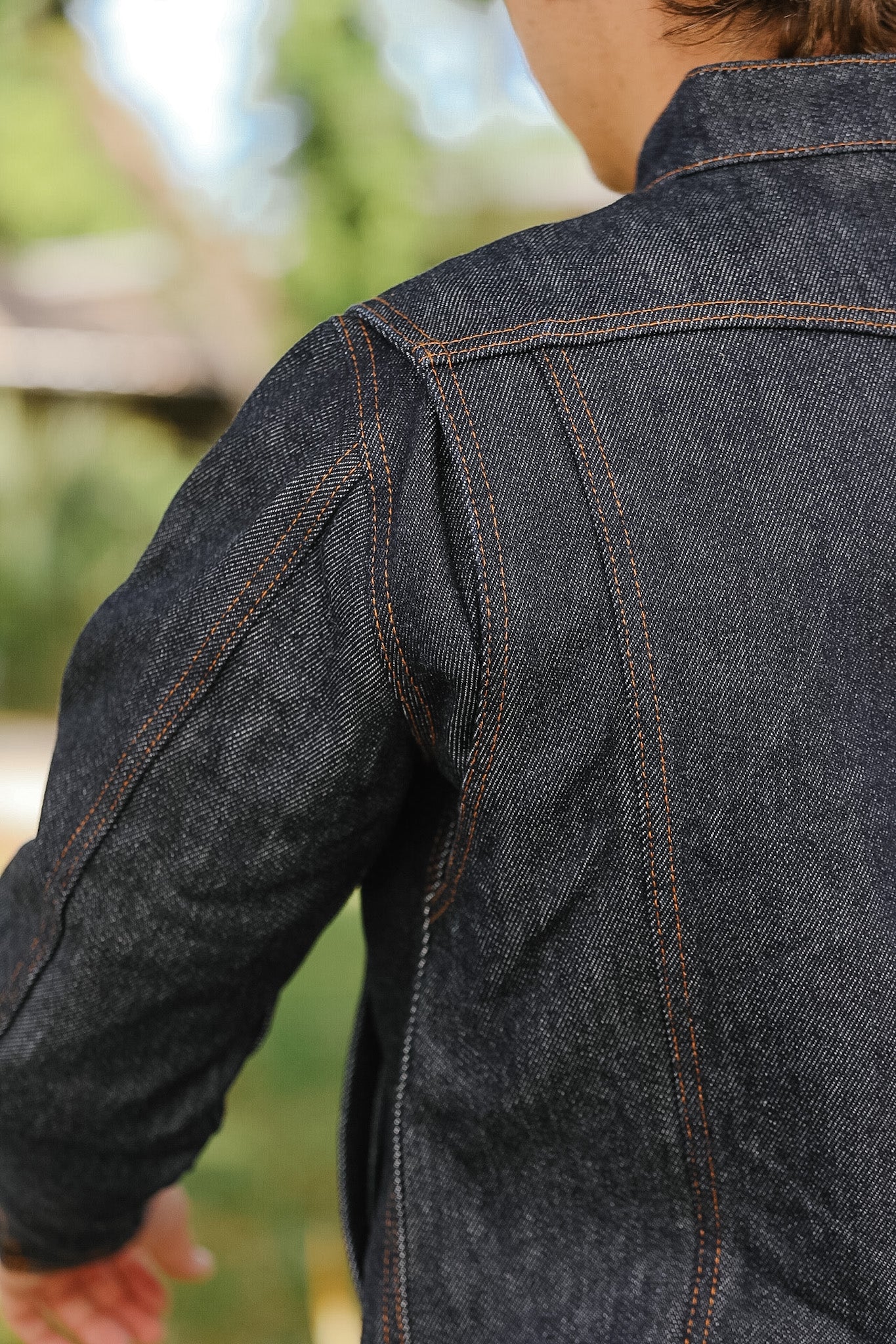Close-up of a person wearing a dark denim jacket with a blurred outdoor background