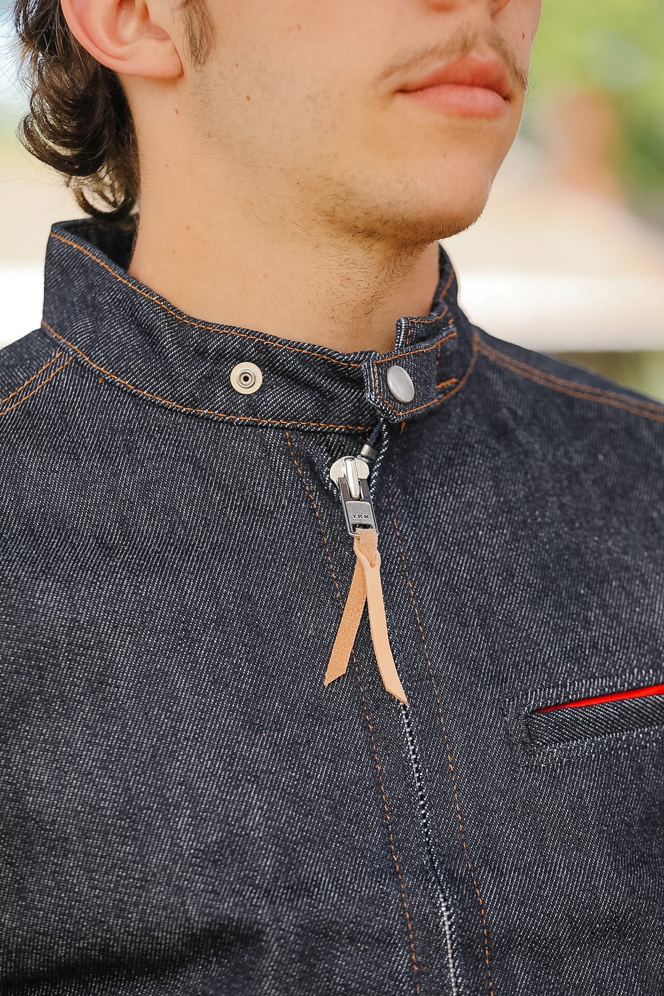Close-up of a person wearing a dark denim jacket with a zipper.