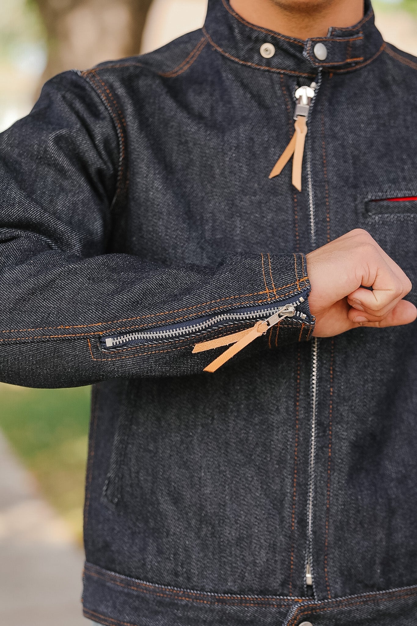 Dark denim jacket with orange zipper pull being unzipped against a blurred natural background