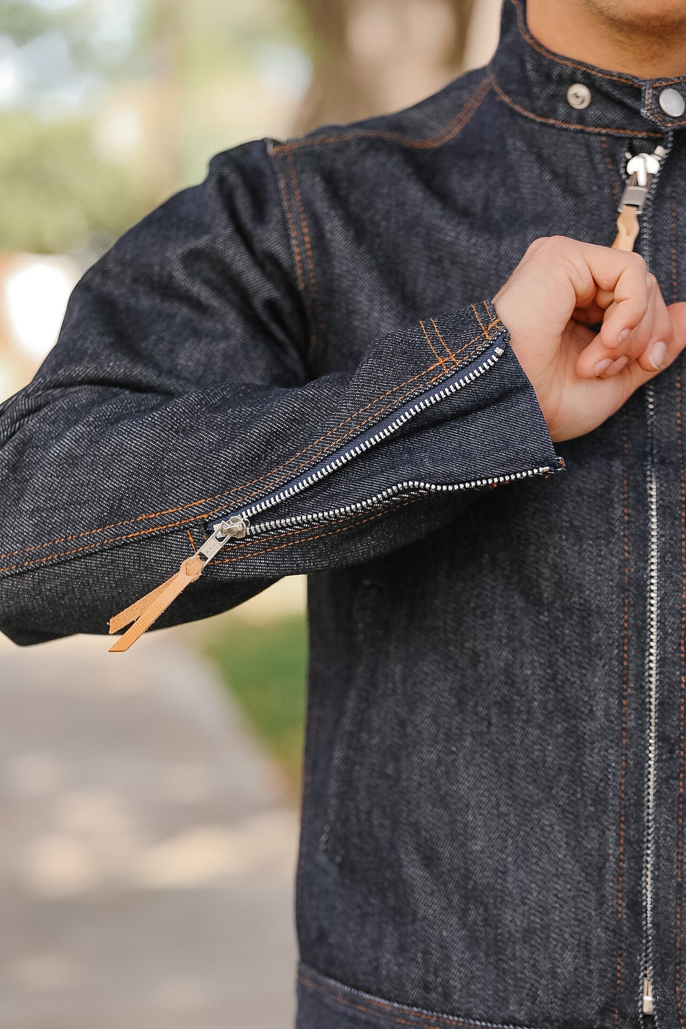 Person wearing a dark denim jacket with zippers, outdoors.