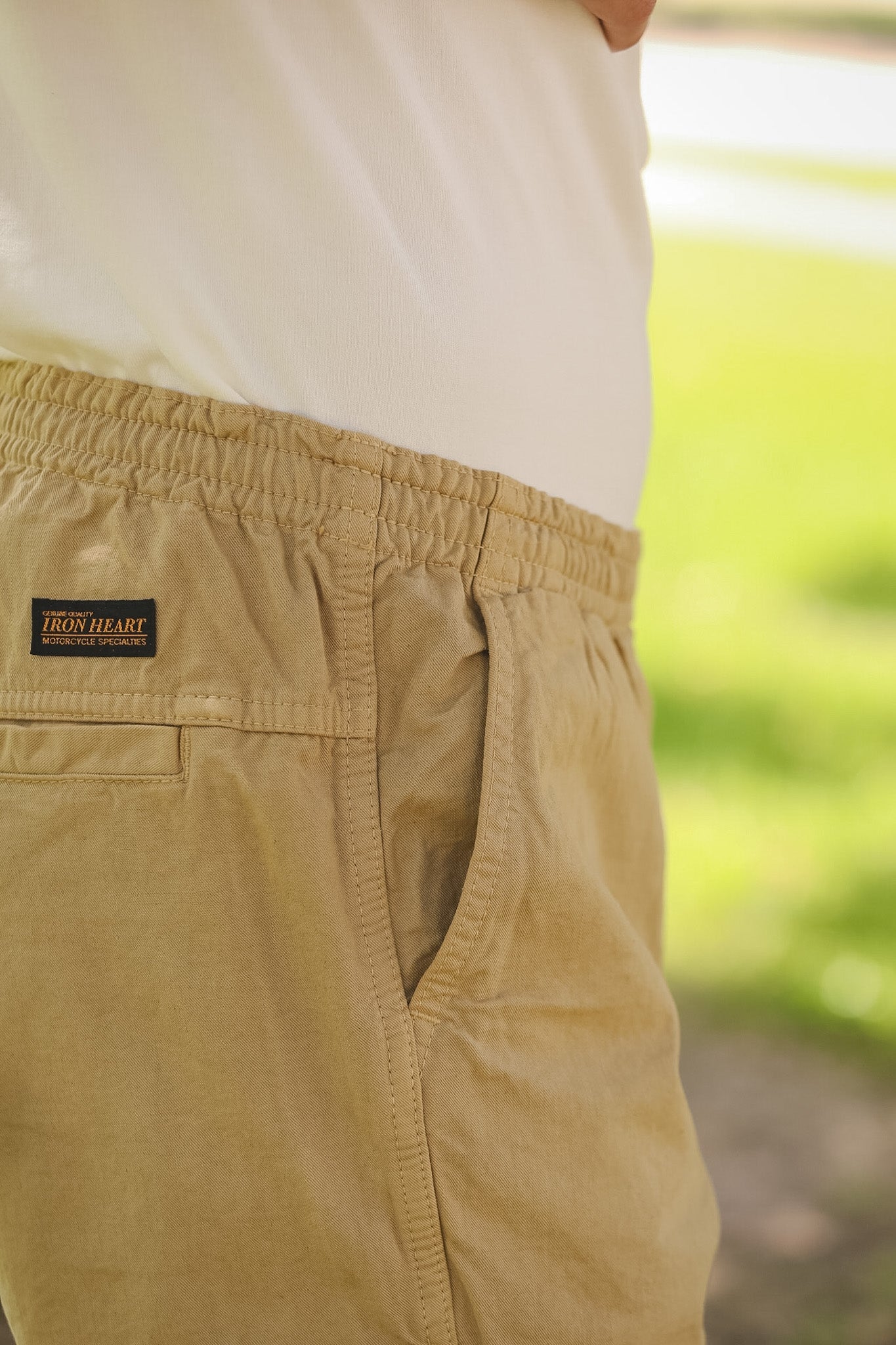 Close-up of beige pants with a brand label against a blurred green background