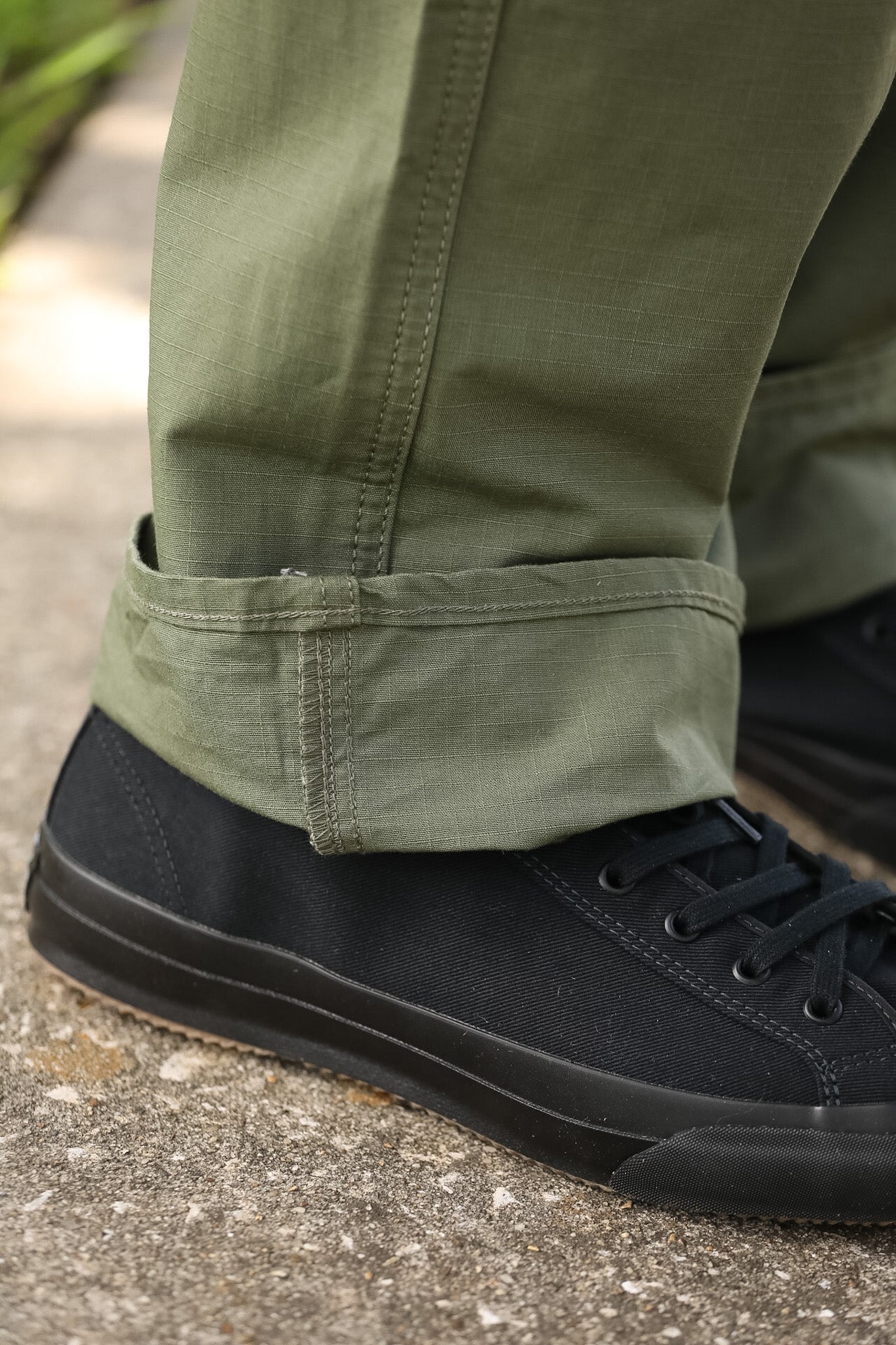 Close-up of green pants rolled up to show black shoes on a concrete surface