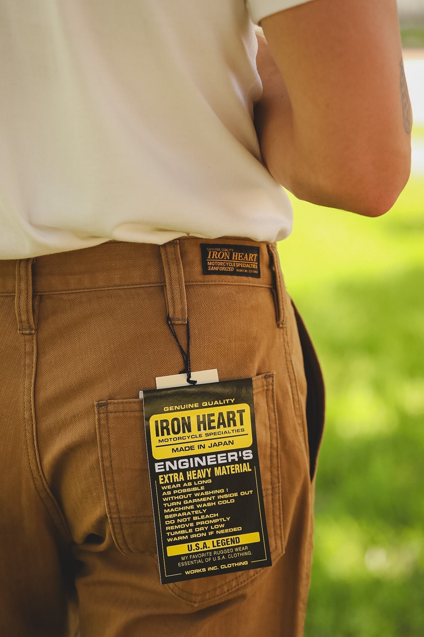 Brown pants with an Iron Heart label on a blurred green background