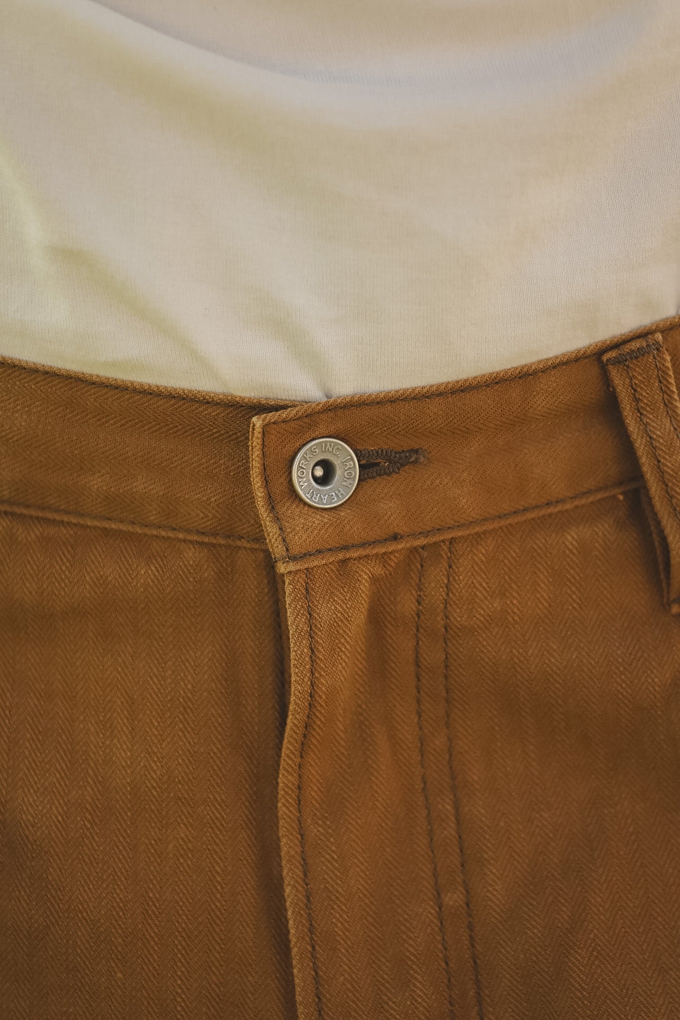 Close-up of brown pants with a button and zipper detail.