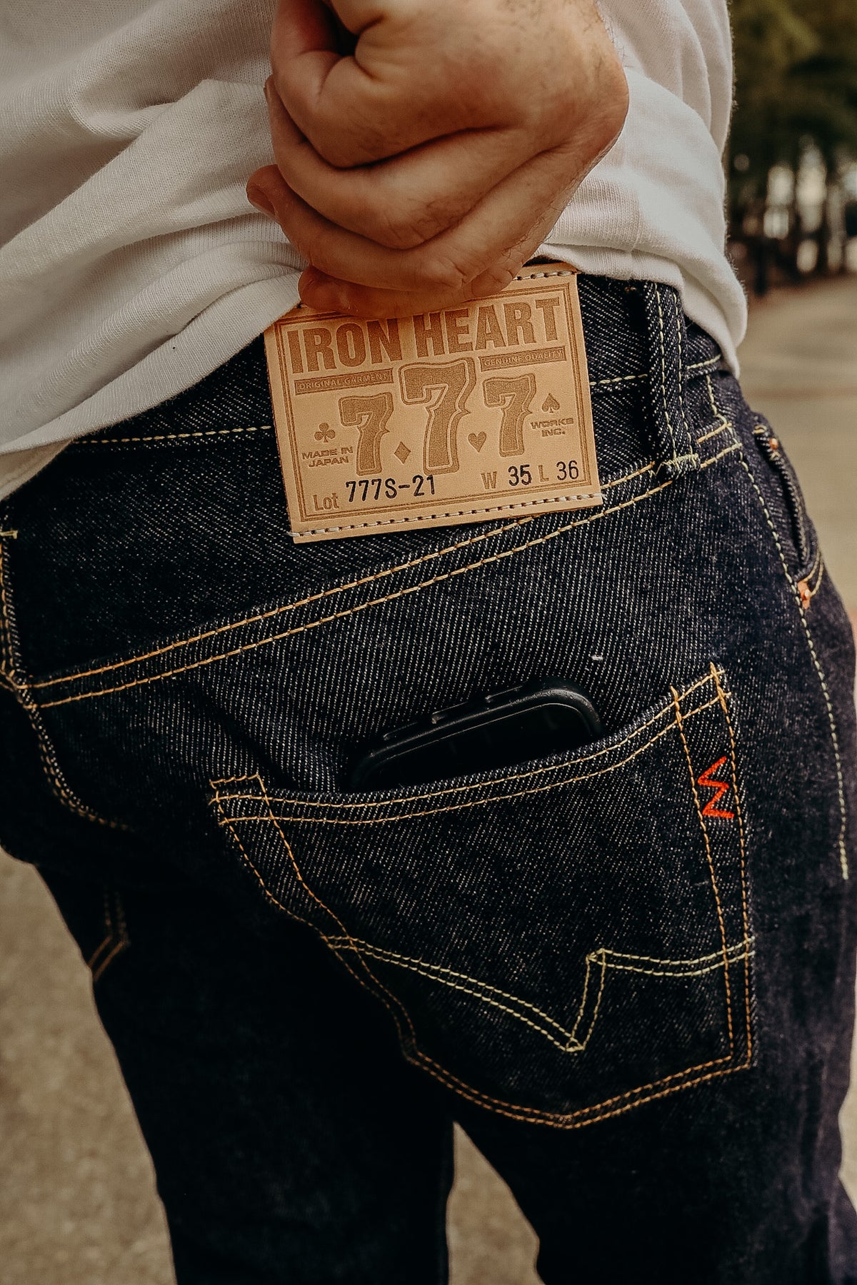A person standing on a sidewalk wearing a white t-shirt and the 21 oz Selvedge Denim Super Slim Tapered Jeans in indigo color with brown shoes.