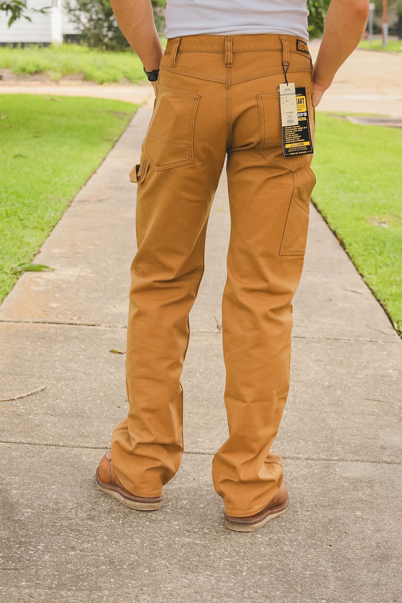 Person wearing brown work pants with a visible brand tag on a sidewalk.