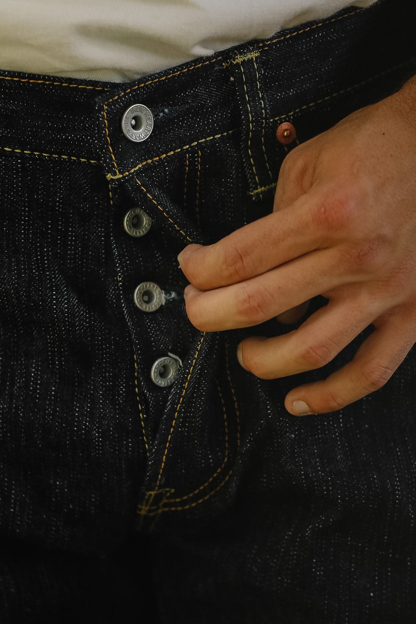 Close-up of a person's hand fastening the front button of dark indigo denim jeans.