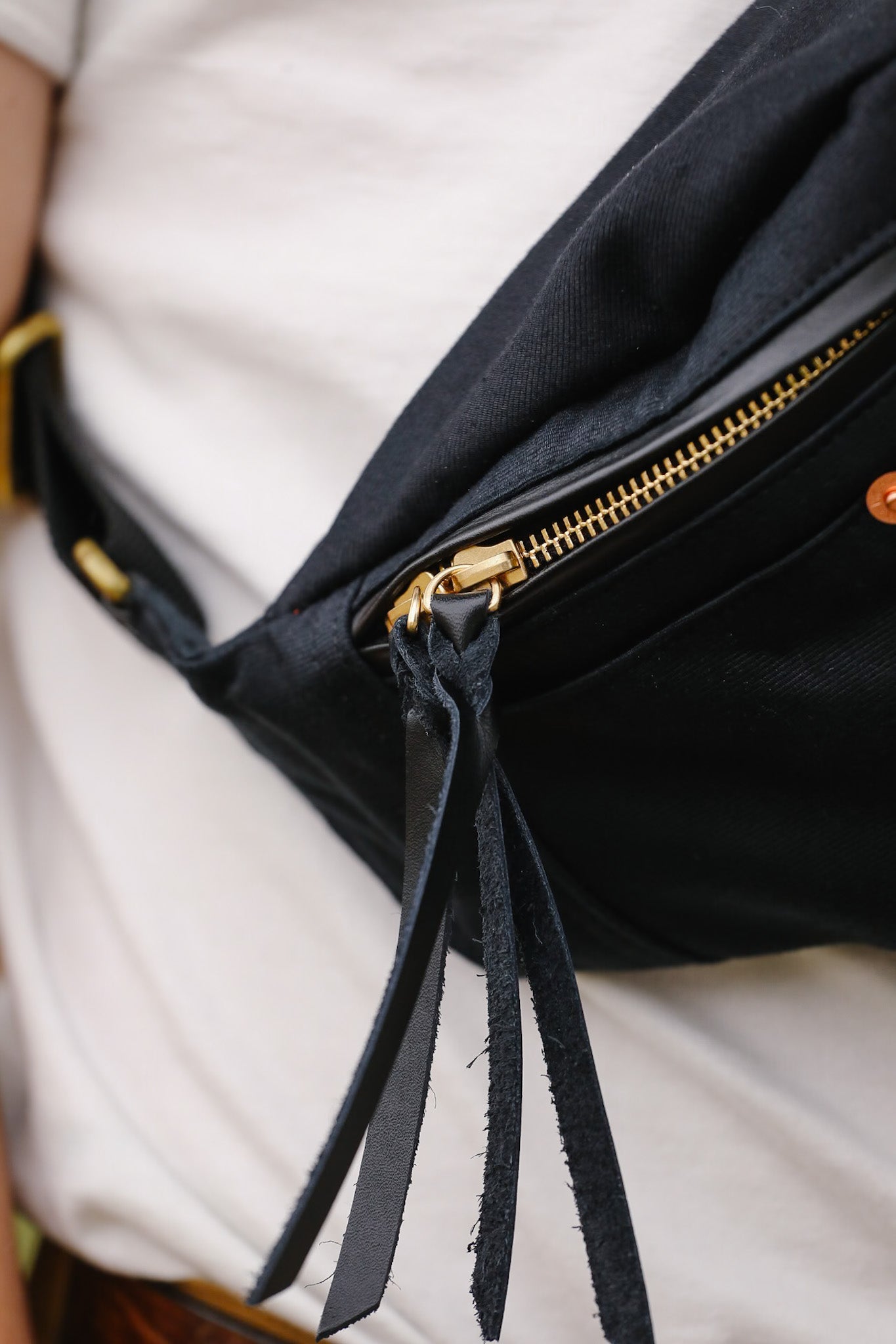 Black waist bag with gold zipper and black drawstring on a white background