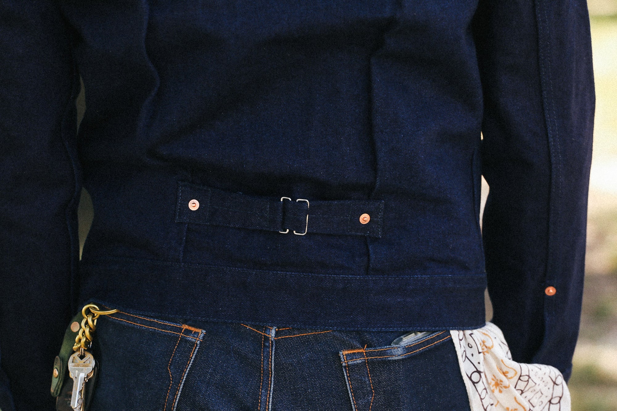 Close-up of a person wearing a dark navy blue denim jacket with a matching fabric belt and silver buckle, paired with dark blue jeans.