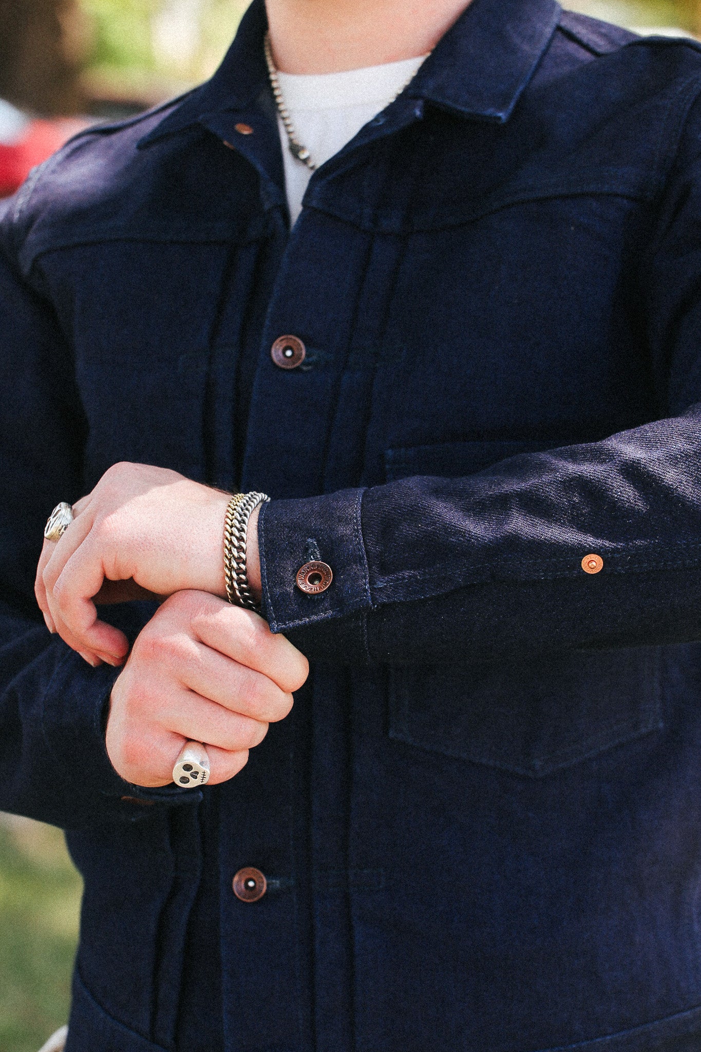 A close-up of a person wearing a dark navy blue corduroy overshirt over a white t-shirt, with silver jewelry on their wrist and hand.