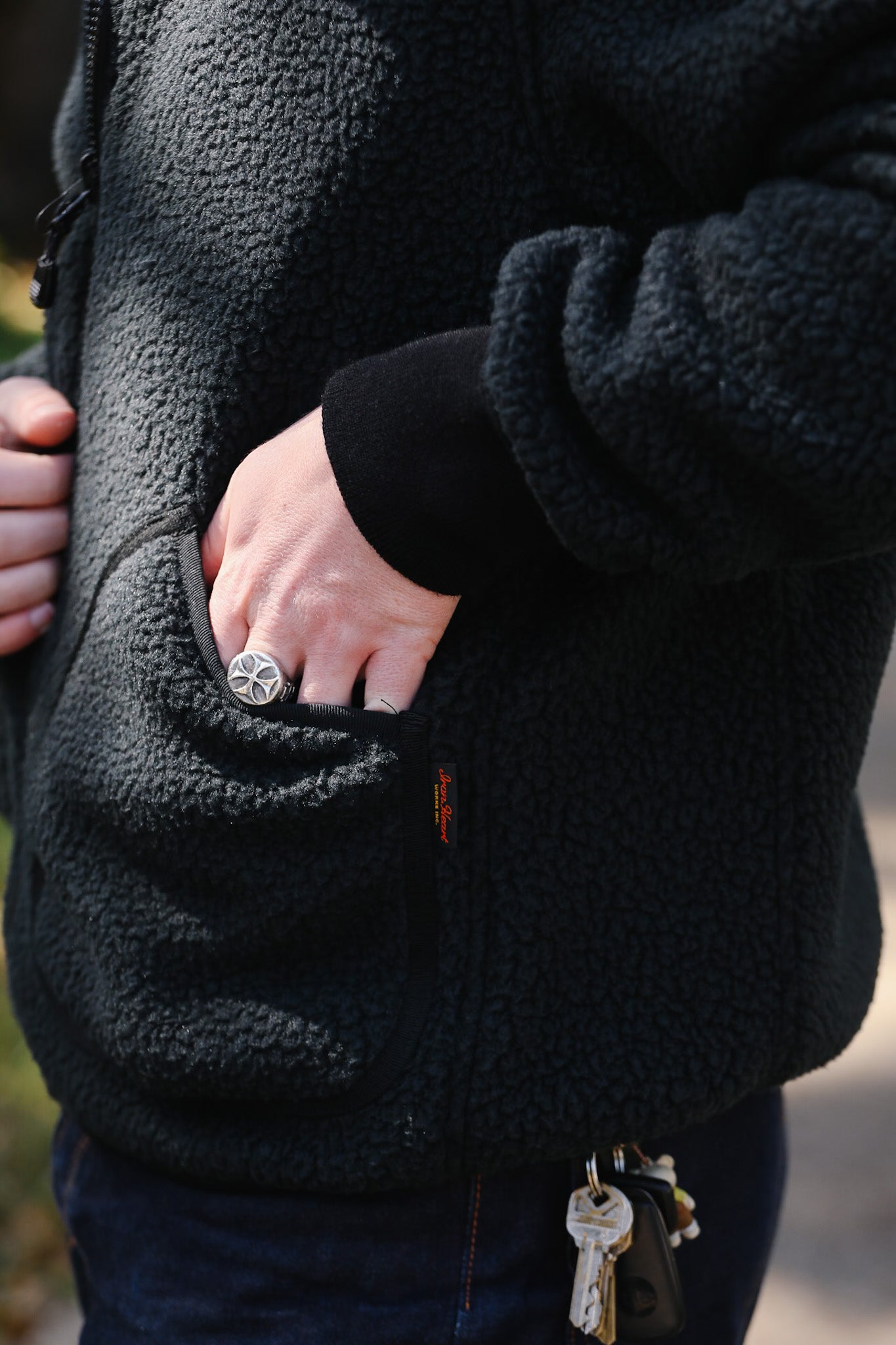 Person wearing a black fleece jacket with a keychain on a blurred background