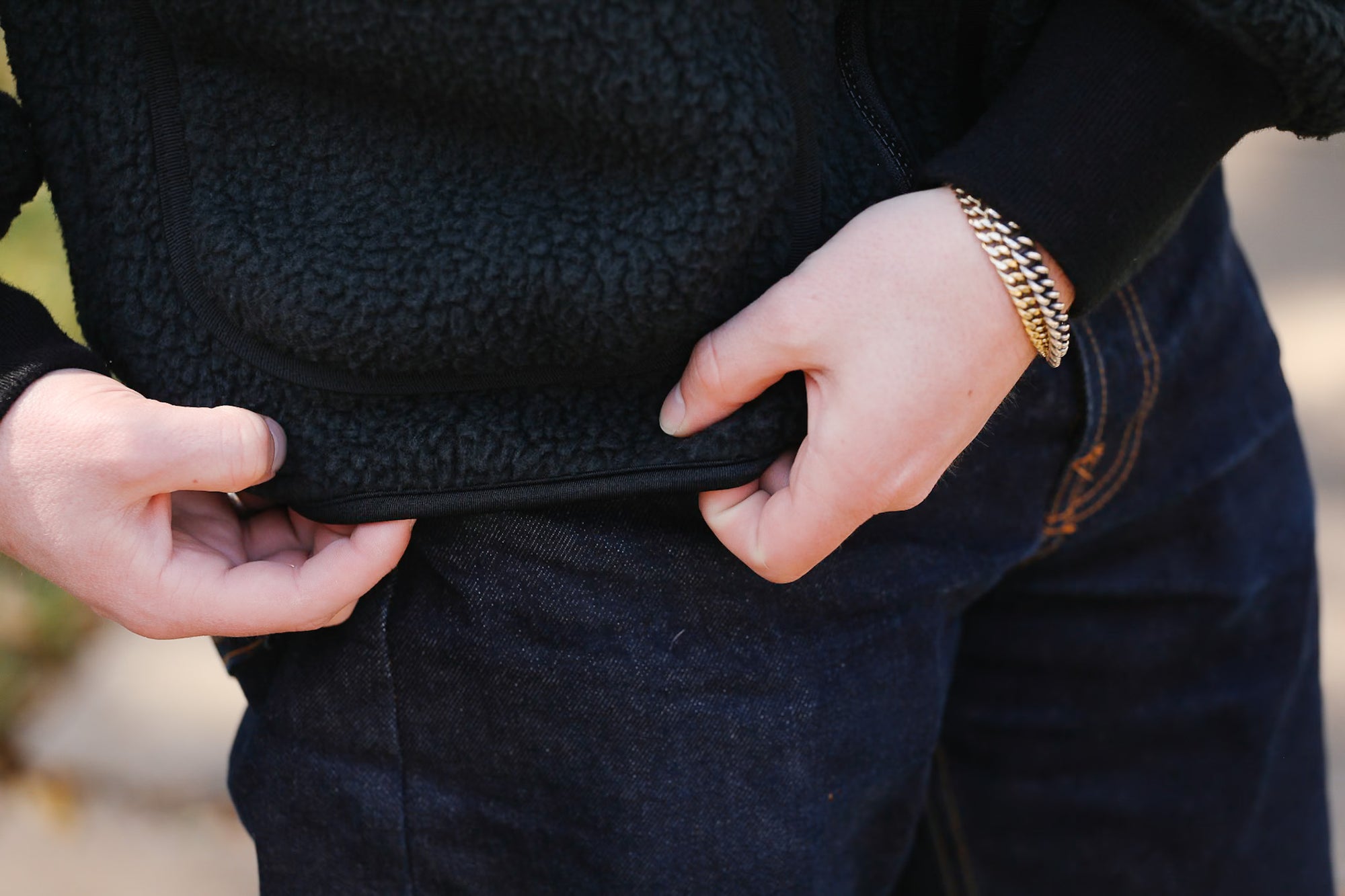 Person wearing a black textured sweater and dark pants with a blurred background