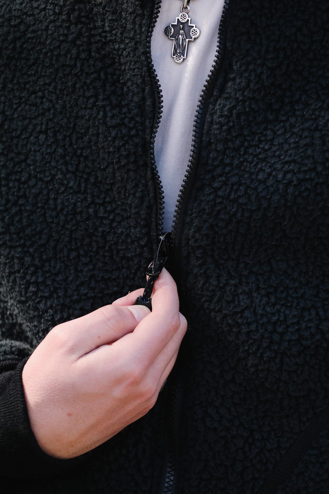 Person zipping a black fleece jacket with a close-up of the zipper mechanism.
