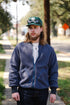 Man wearing a blue fleece jacket and green cap outdoors on a sidewalk.