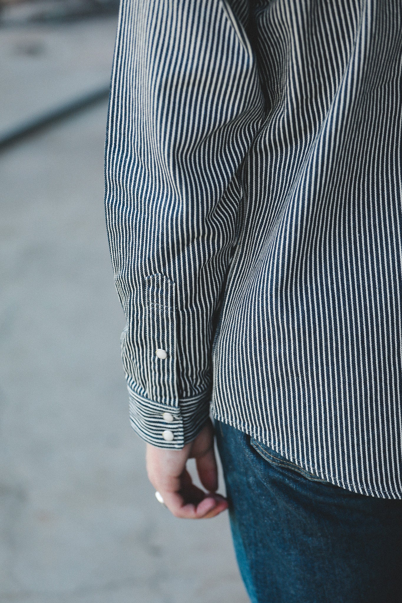 Close-up of a person wearing a navy and white vertically striped long-sleeve button-up shirt with dark blue jeans, shown from the back.