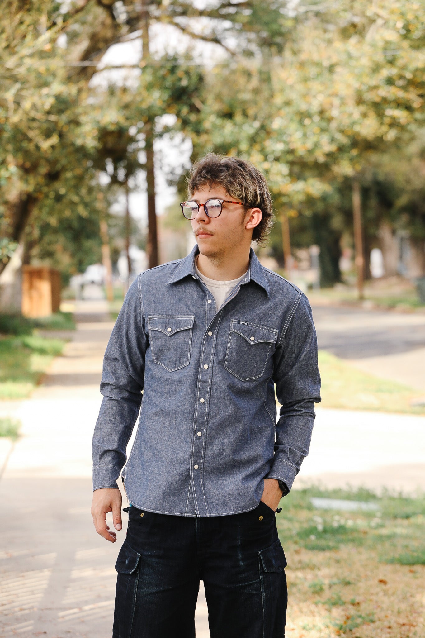 Man wearing a denim shirt outdoors with trees in the background
