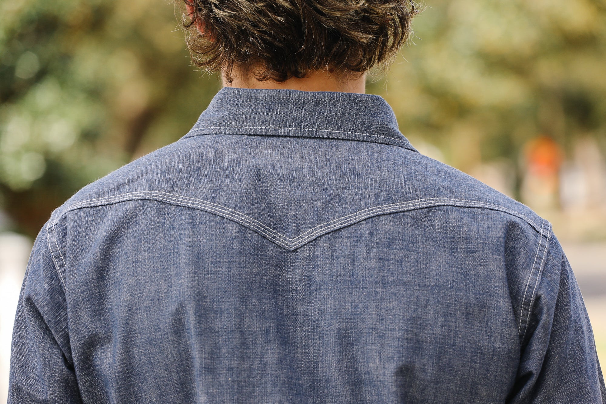 Person wearing a blue denim shirt with a blurred outdoor background
