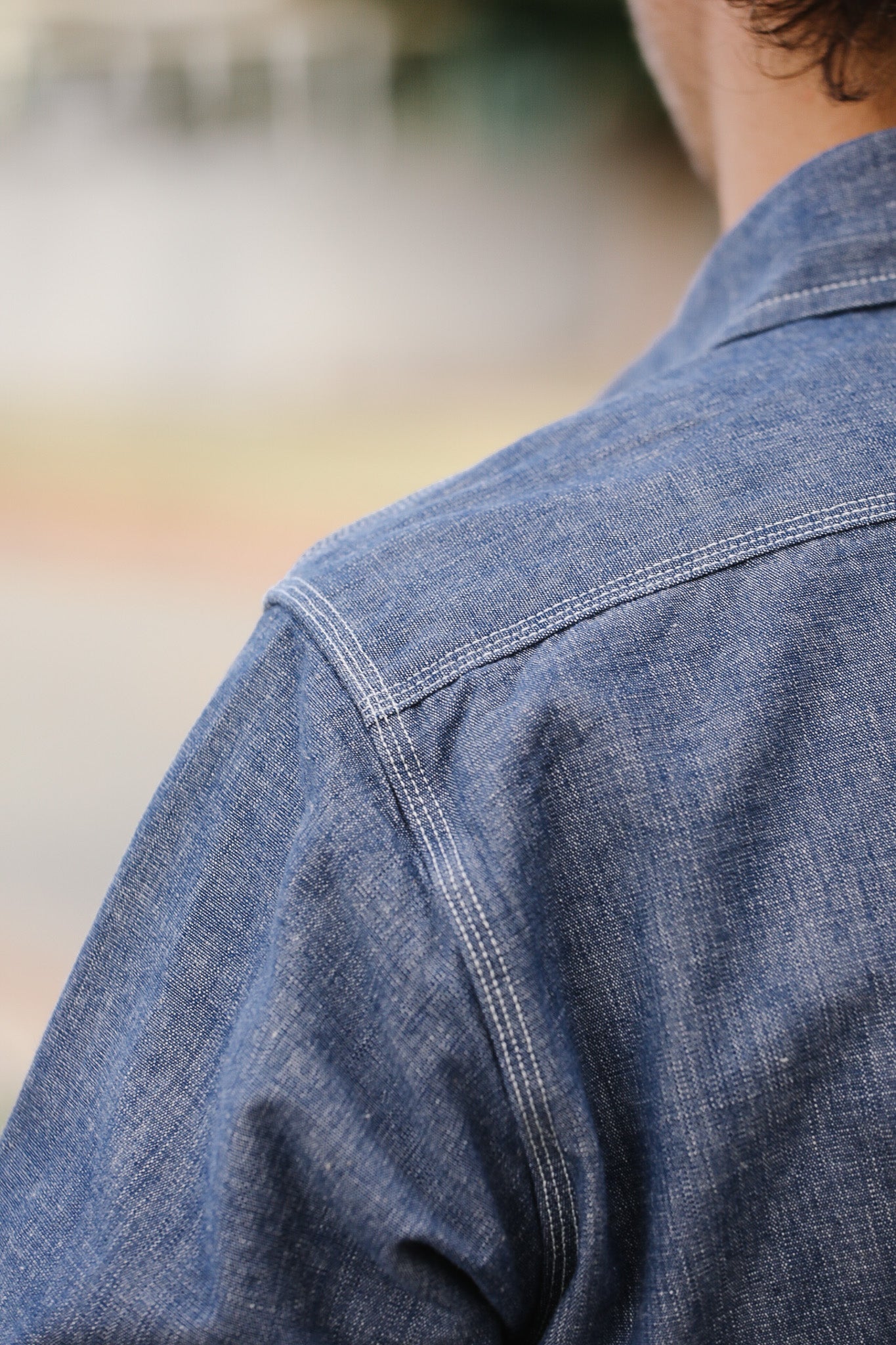 Close-up of a person wearing a blue denim shirt with a blurred background