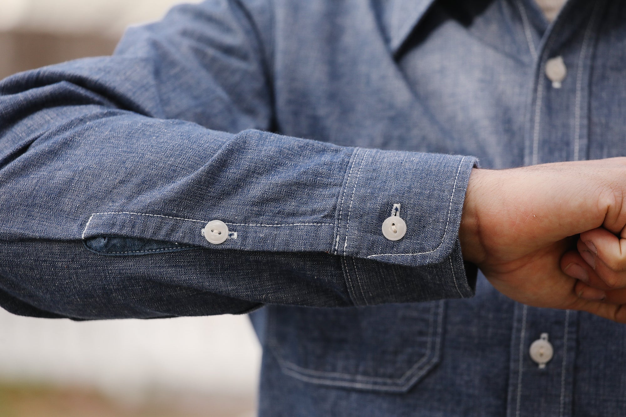 Close-up of a person wearing a blue denim shirt with rolled-up sleeves.