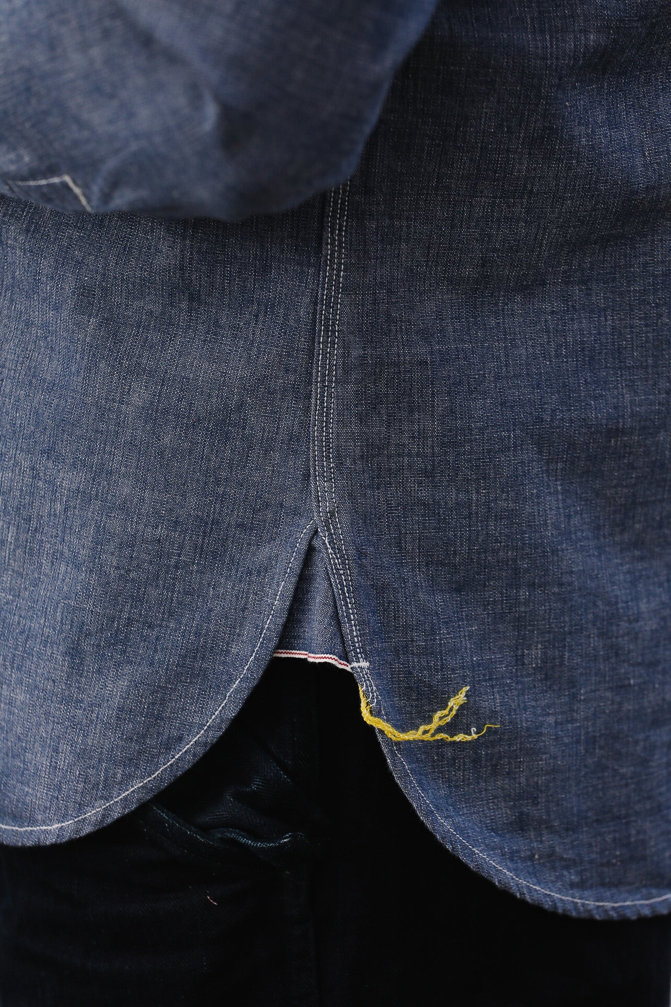 Close-up of a blue denim fabric with a yellow thread, possibly indicating a repair or stitching detail.