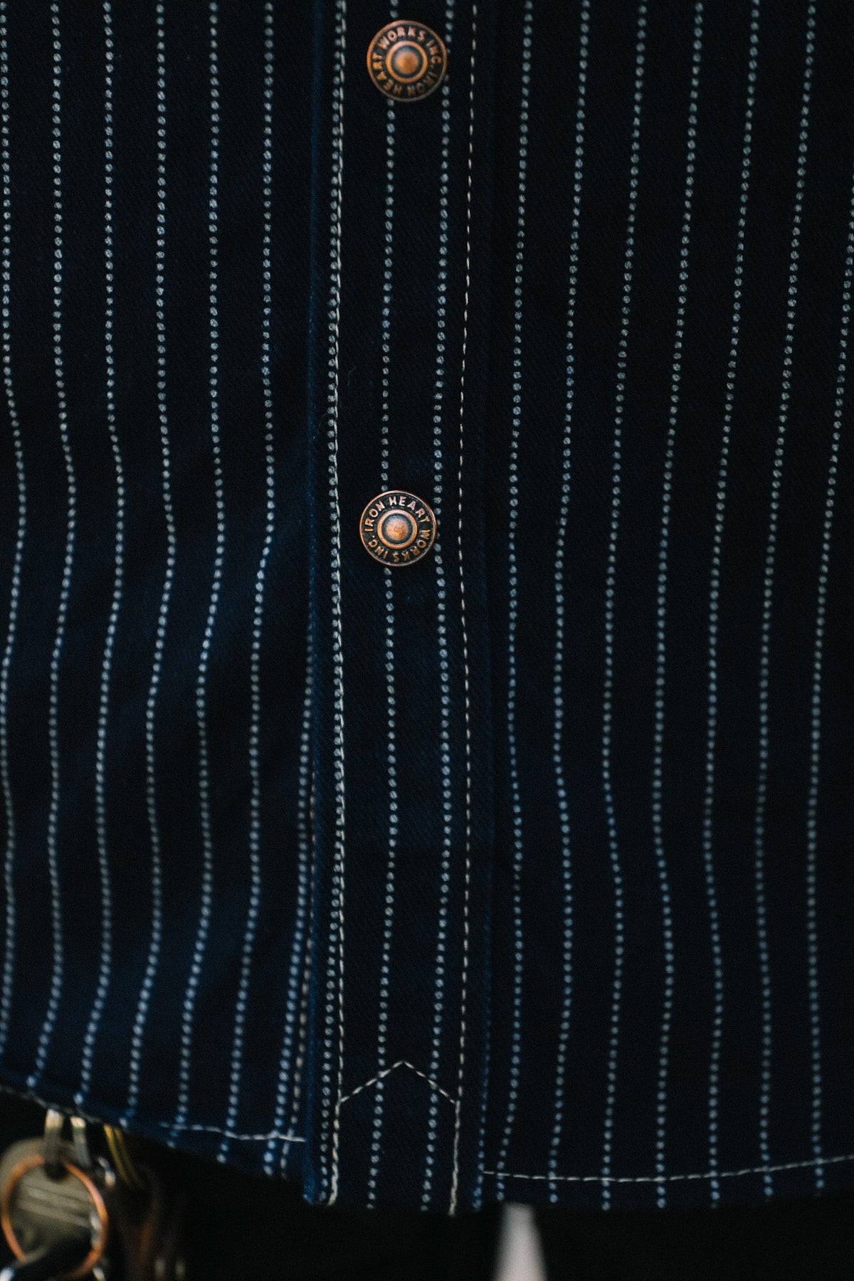 Close-up of a dark navy pinstriped shirt jacket with vertical white stripes and decorative round copper-toned buttons.