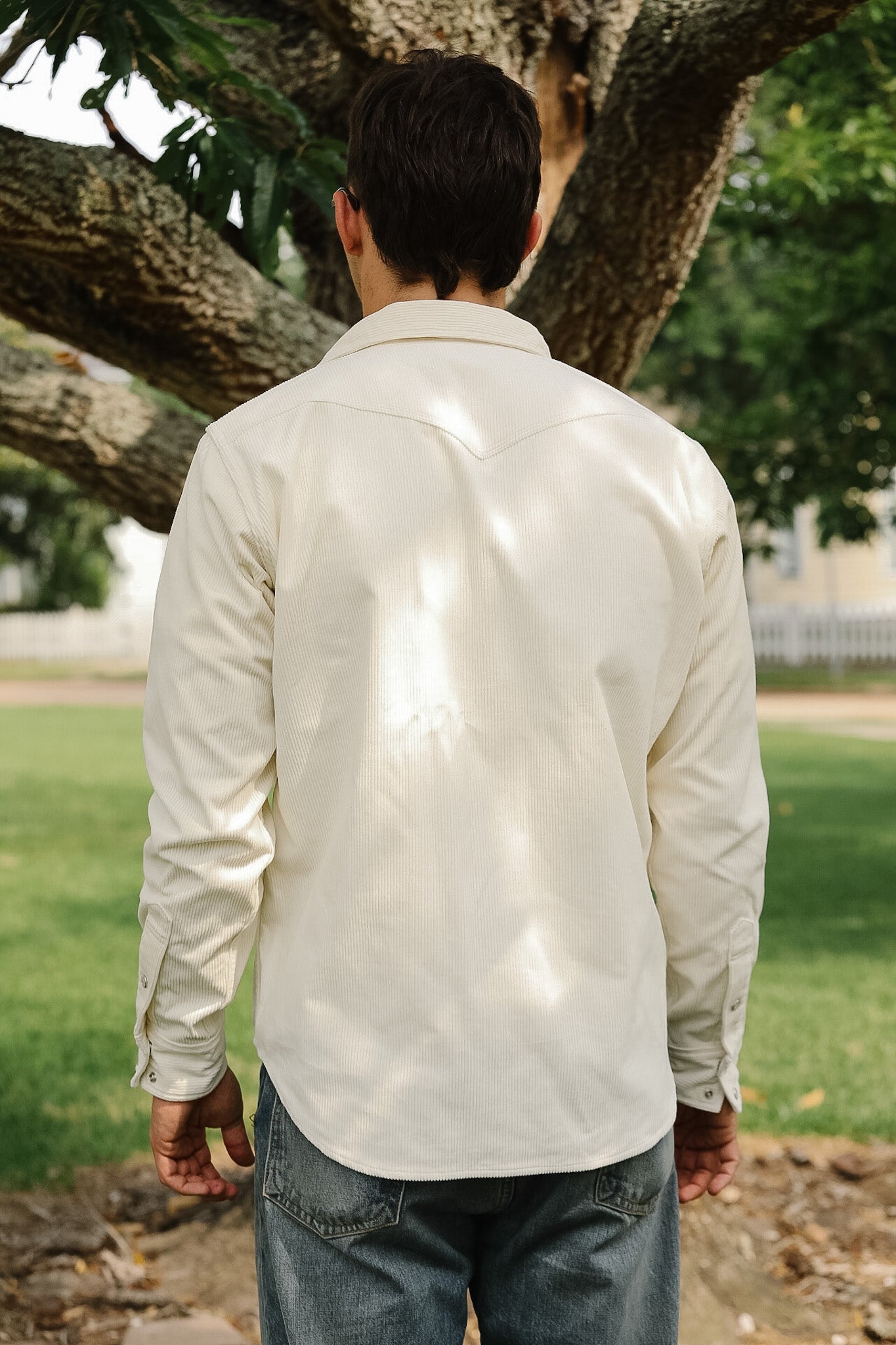 Person wearing a light-colored shirt standing under a tree in an outdoor setting