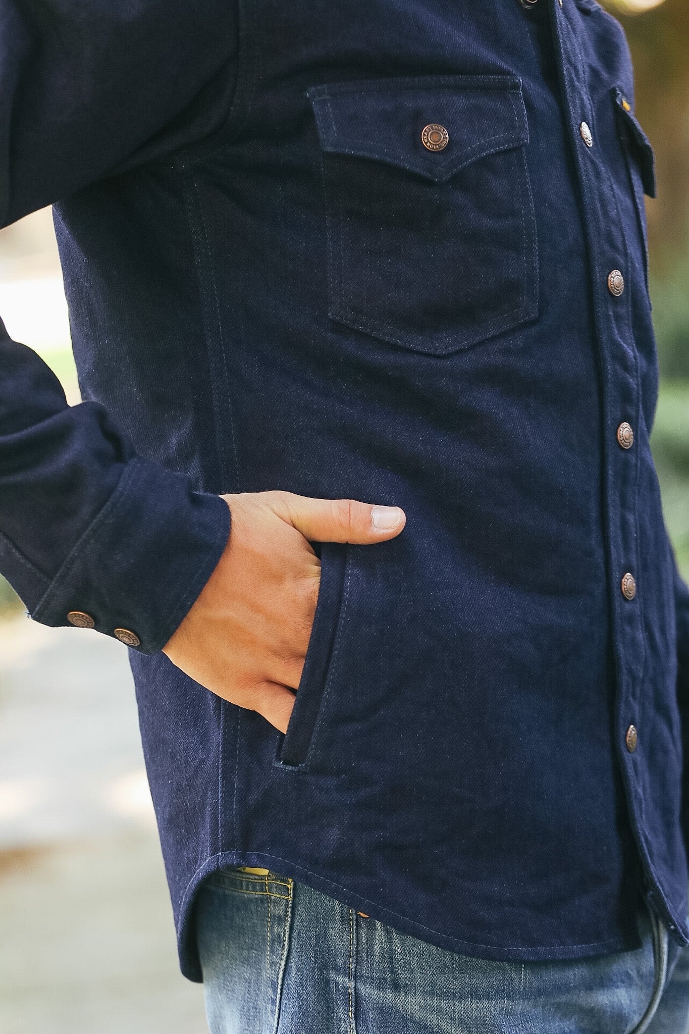 Close-up of a person wearing a dark navy corduroy button-up shirt with a chest pocket and side pocket, paired with blue jeans.