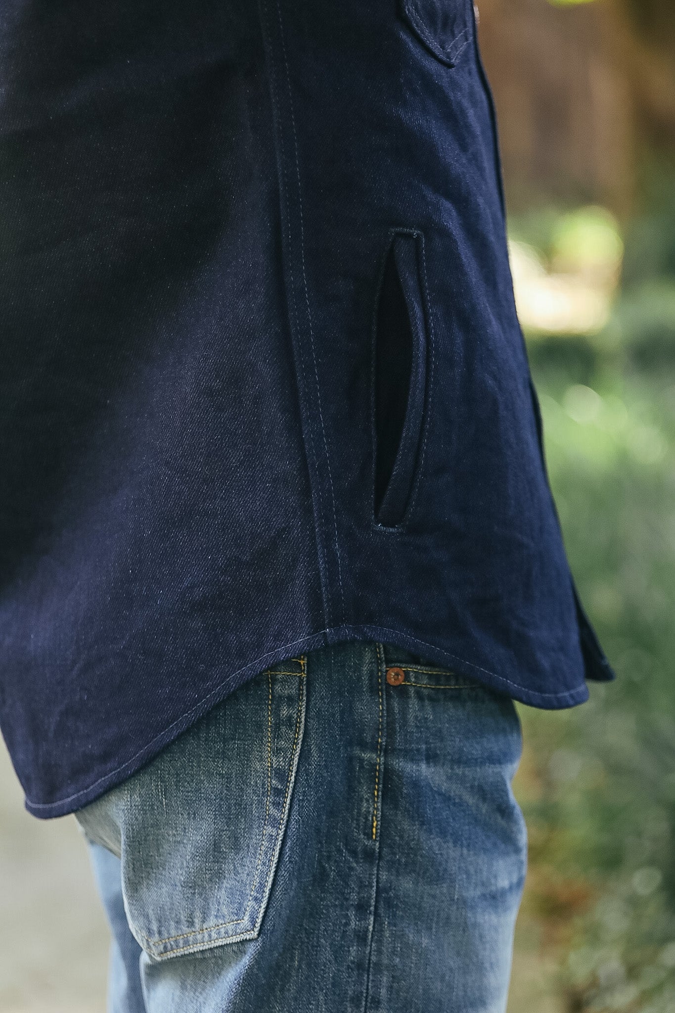 Close-up of a person wearing a dark navy blue corduroy jacket with a side welt pocket, paired with blue jeans in an outdoor setting.