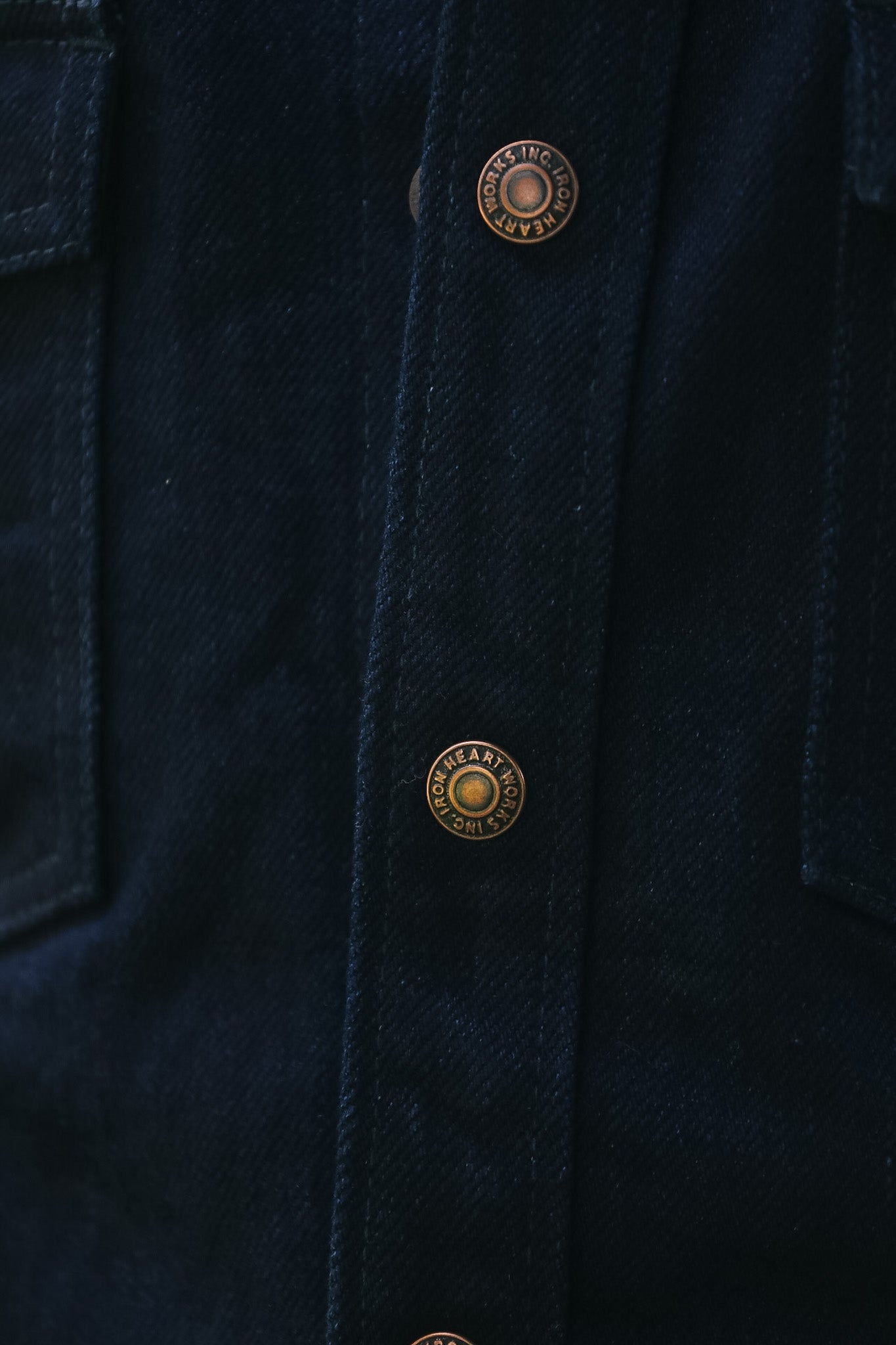 Close-up of a dark navy blue denim jacket showing the button placket with bronze-toned metal buttons.