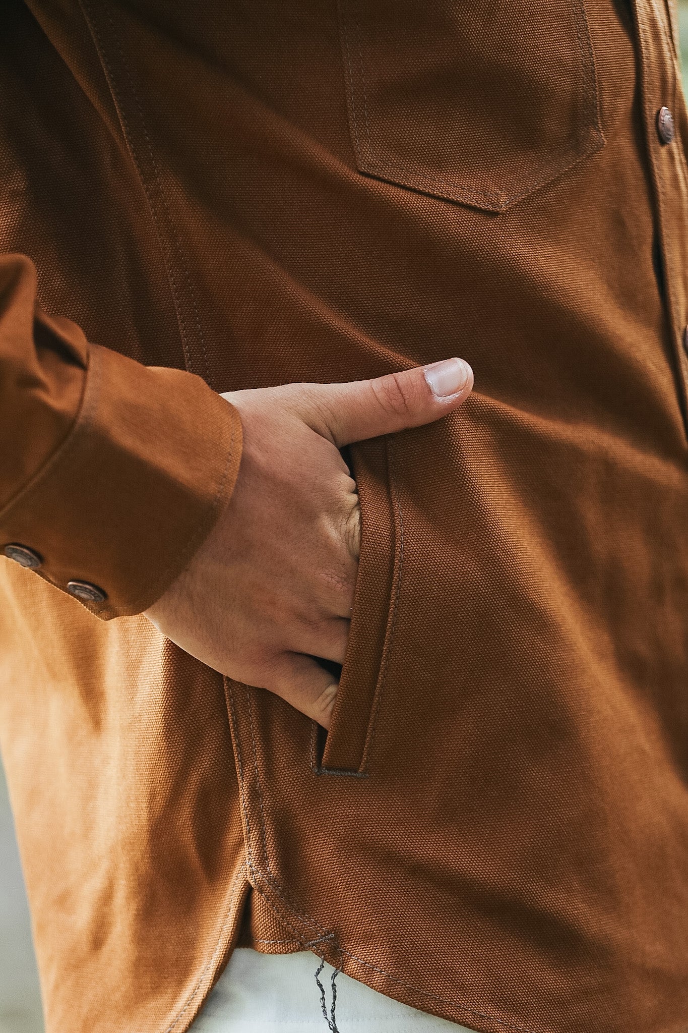 Close-up of a person wearing a warm brown suede or velvety button-front jacket, with one hand reaching into a side pocket.