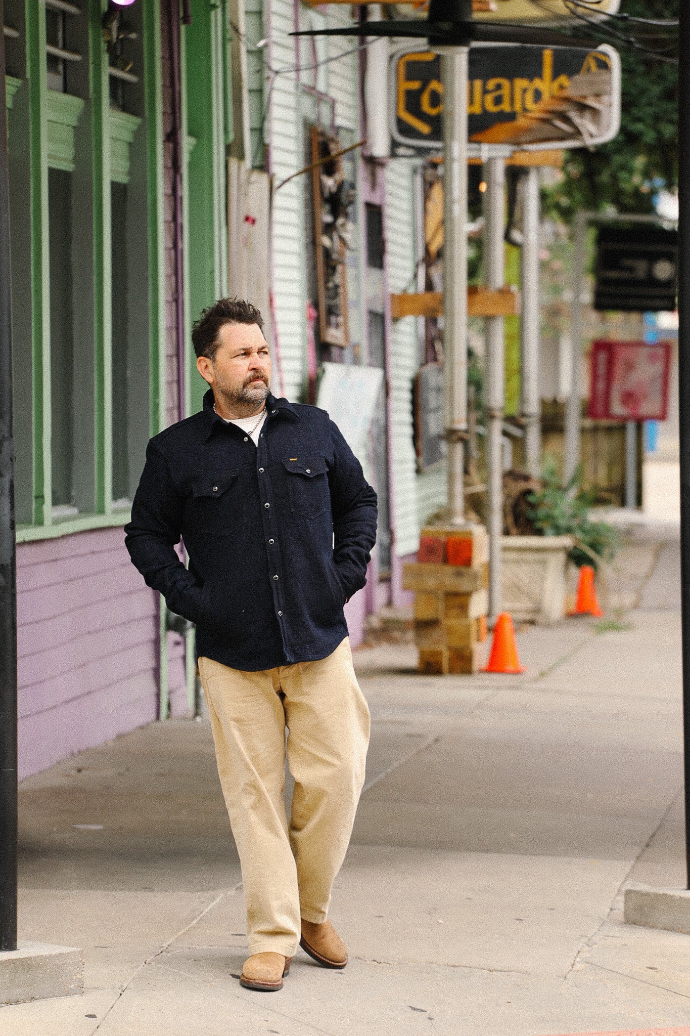 Man walking on a city street wearing a dark jacket and beige pants.