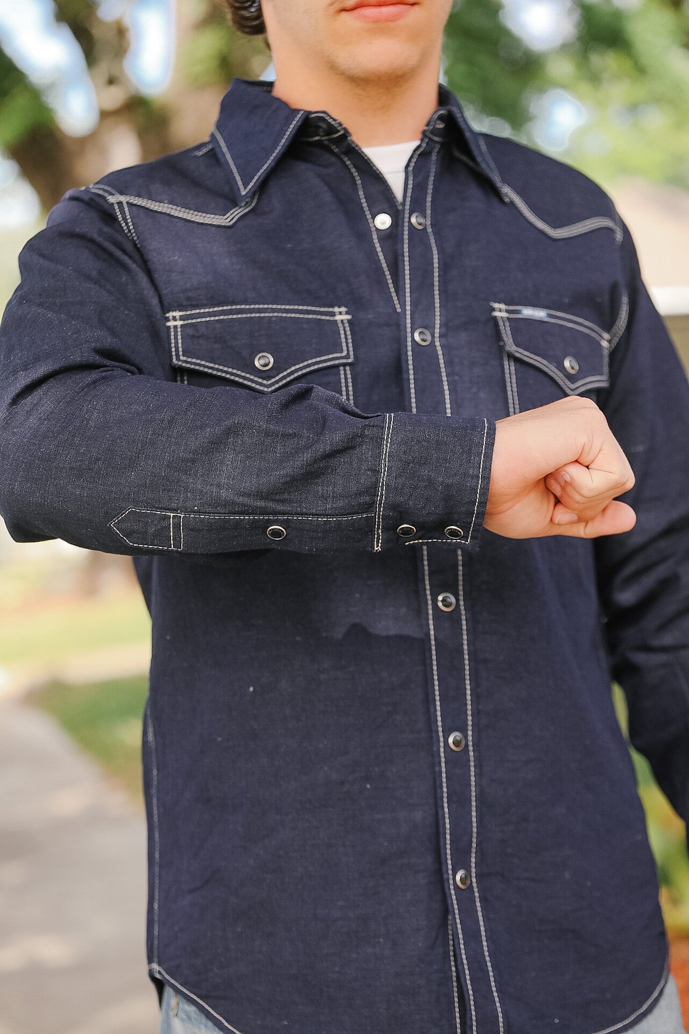 Person wearing a dark denim jacket with white stitching outdoors