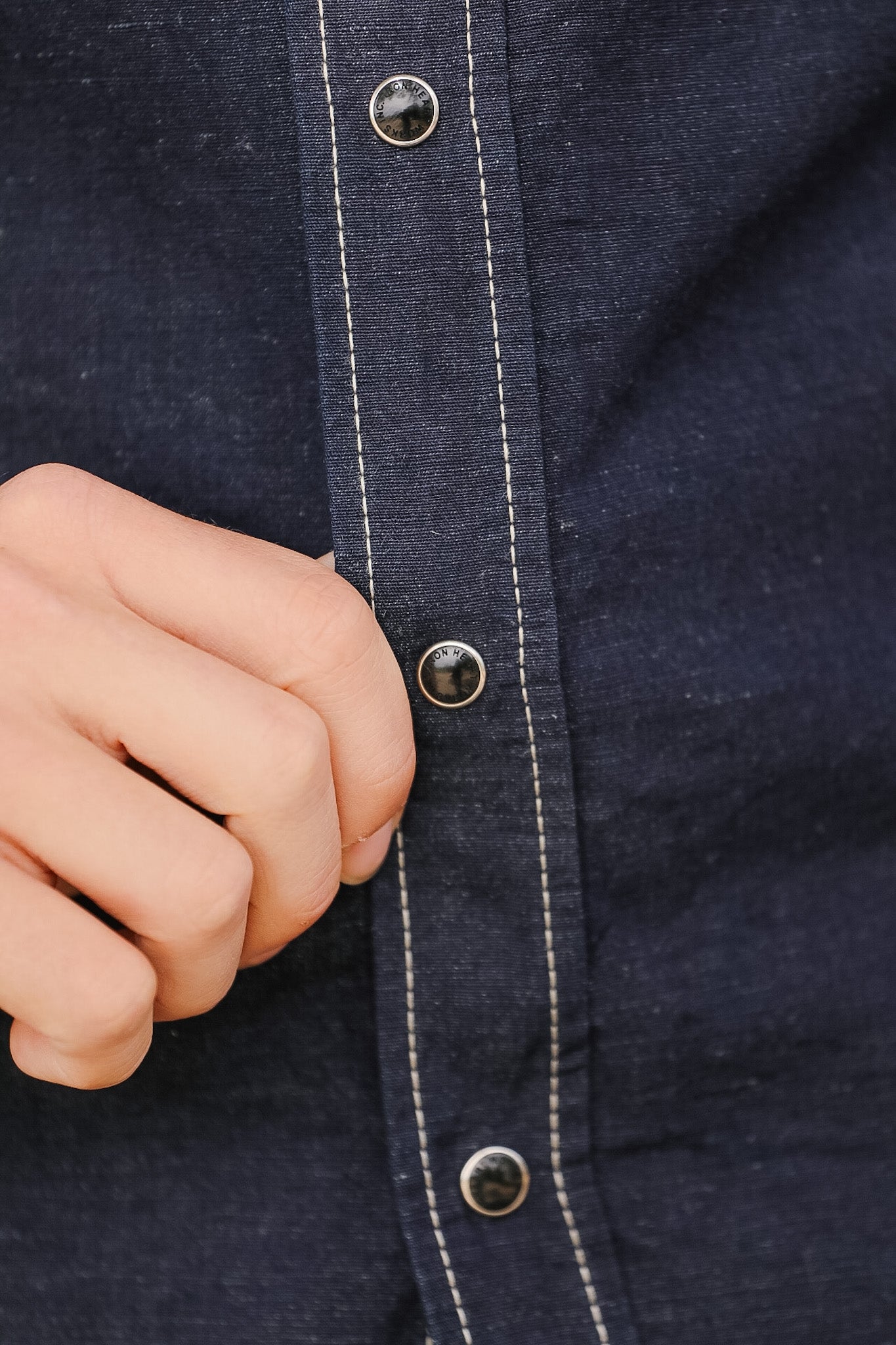 Close-up of a person wearing a dark blue denim shirt with buttons, focusing on the fabric texture and button details.