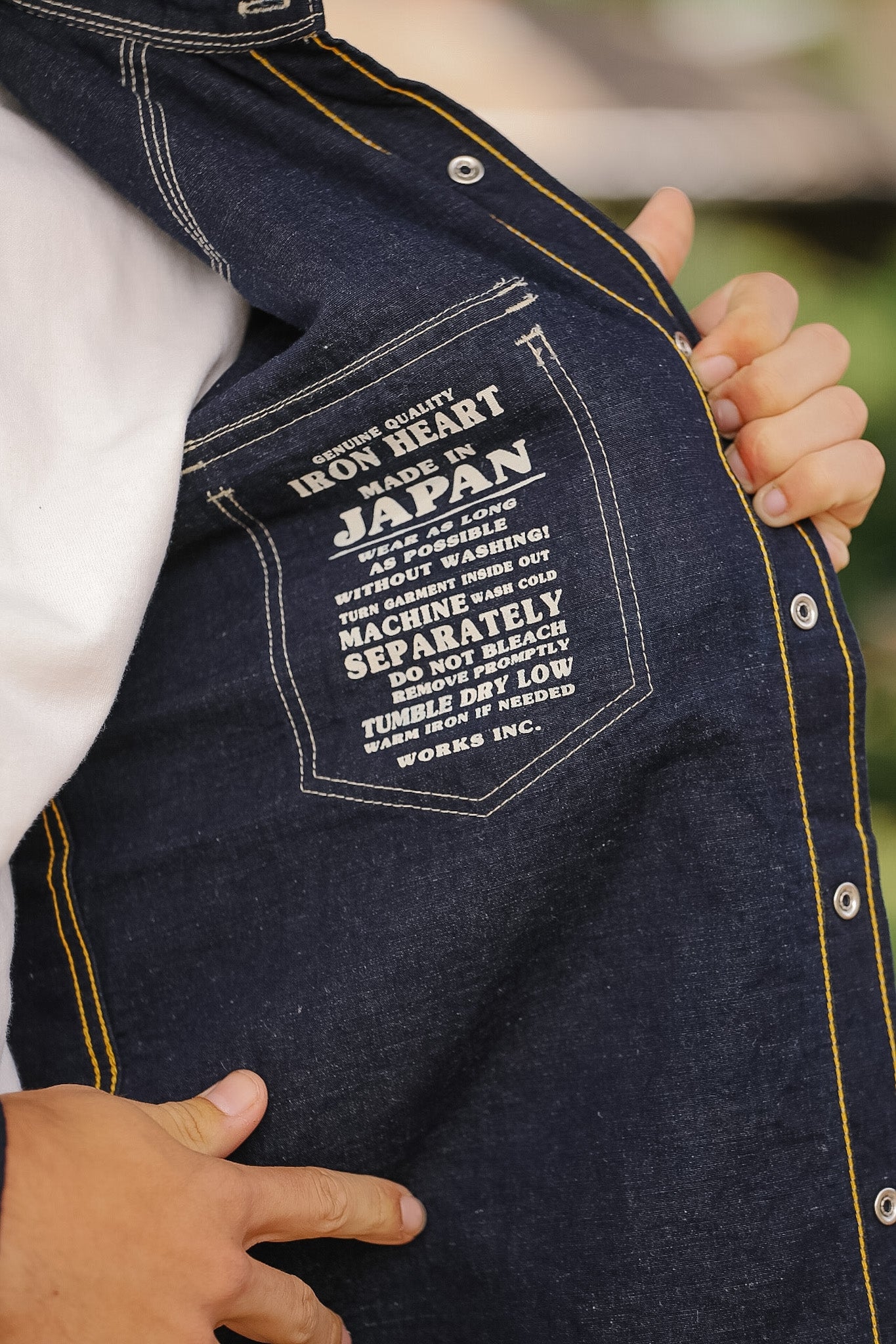 Denim jacket with a label on the chest held by hands against a blurred background