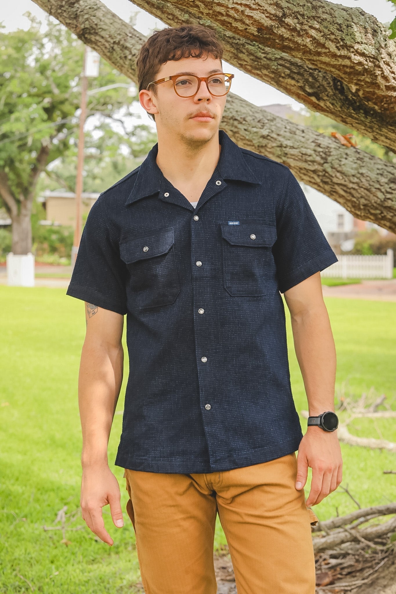 Person wearing a navy shirt and brown pants standing outdoors near a tree