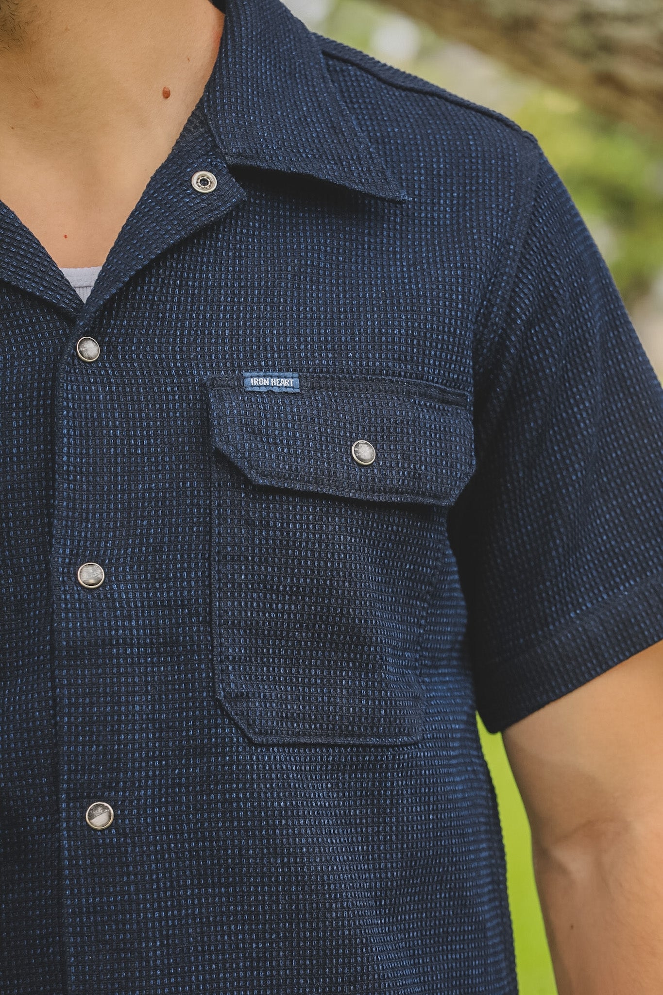 Navy blue short-sleeve shirt with button details on a blurred natural background