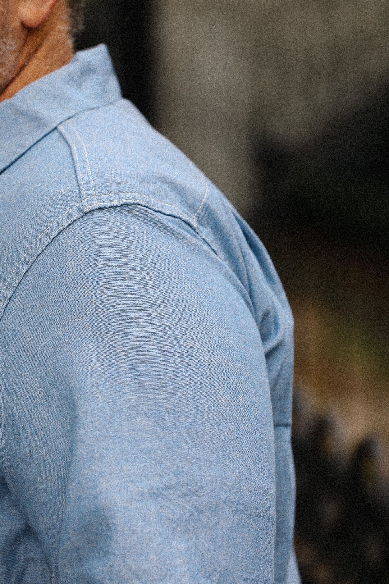 Close-up of a person wearing a light blue denim shirt with a blurred background