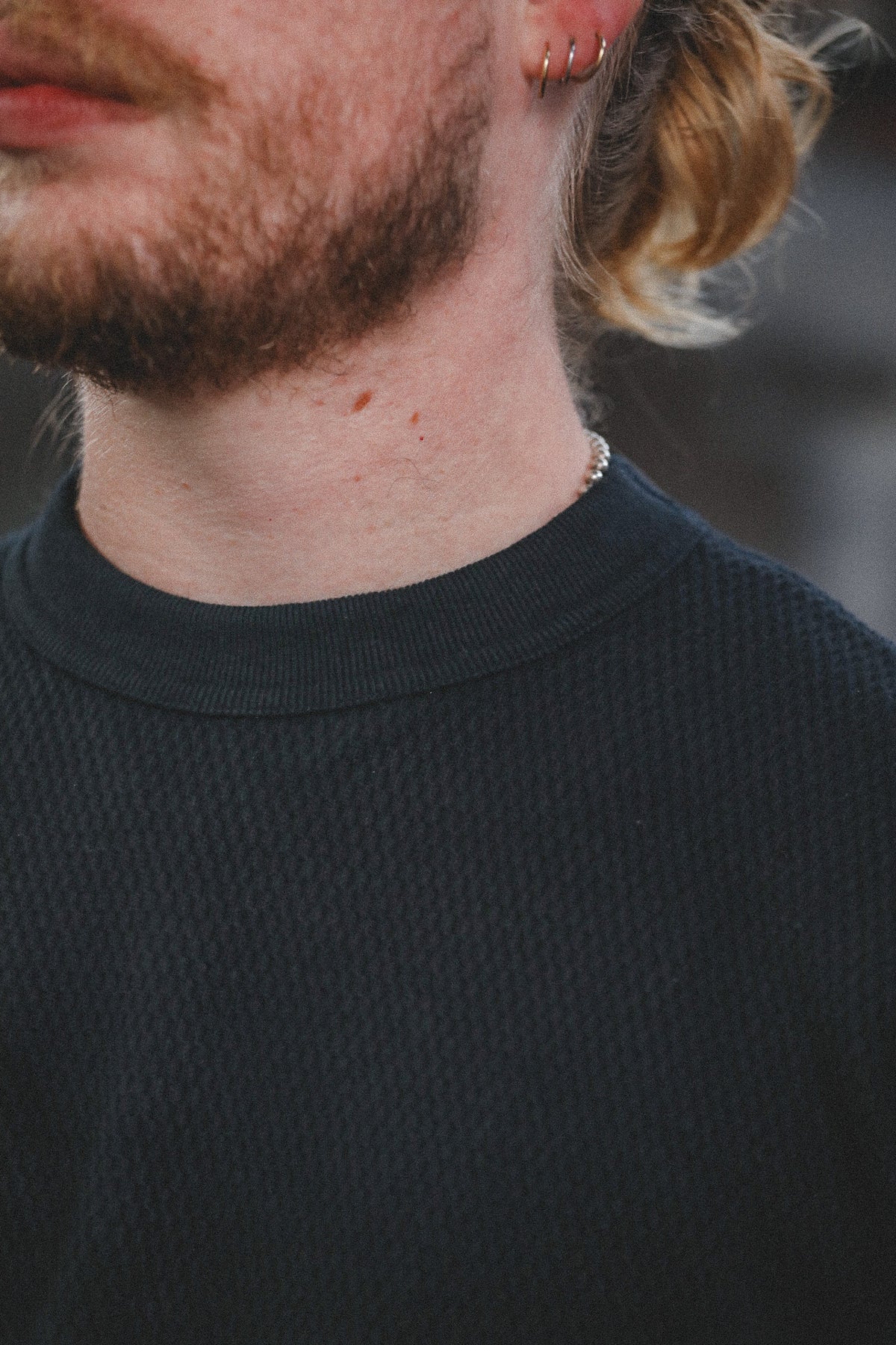 Close-up of a man's neck and lower face wearing a dark charcoal gray textured crewneck sweater.